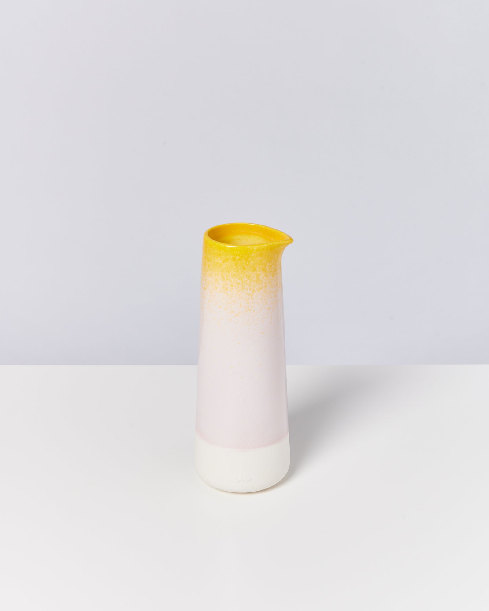 Keramikkrug mit gelbem Rand und weißem Körper auf weißem Hintergrund.