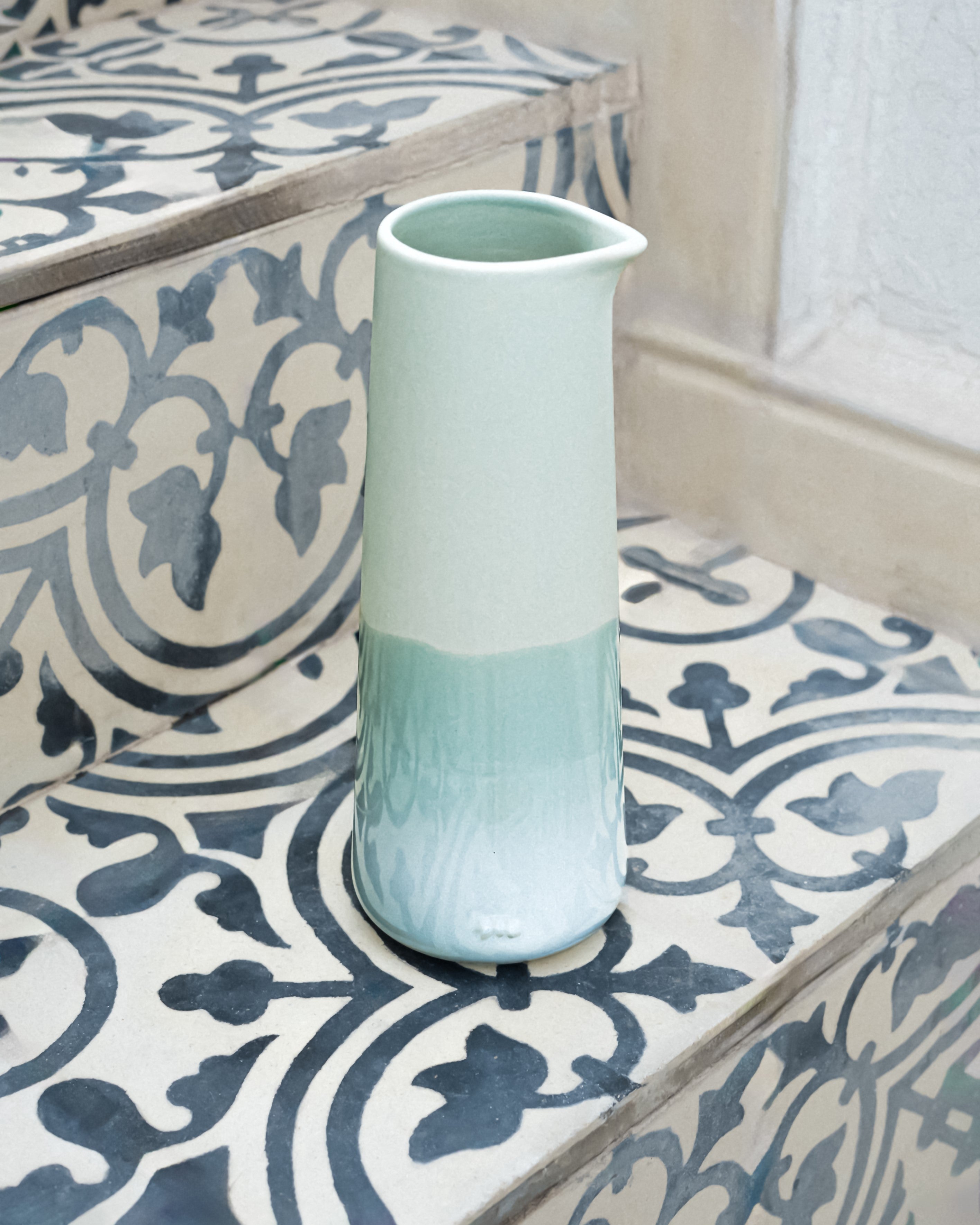 Ein pastellfarbener Krug steht auf einer Treppe mit gemusterten Fliesen.