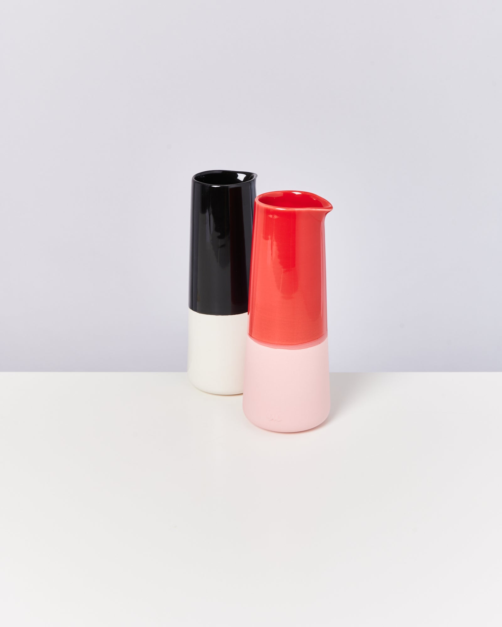 Zwei minimalistische Keramikvasen, eine rot und eine schwarz-weiß, stehen auf einer weißen Oberfläche.