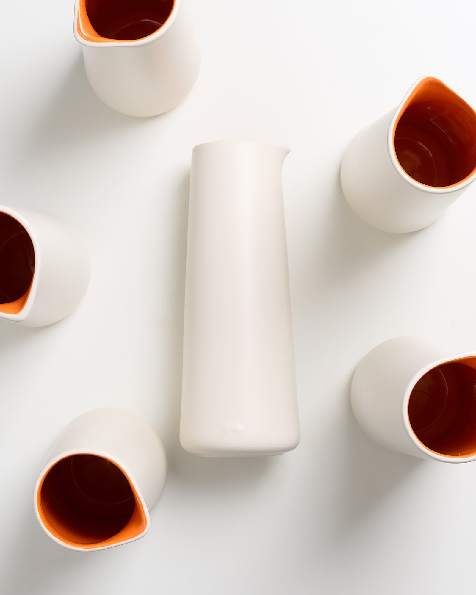 Sechs weiße Keramikkrüge mit orangem Inneren, einer größer und in der Mitte liegend, auf einem weißen Hintergrund.