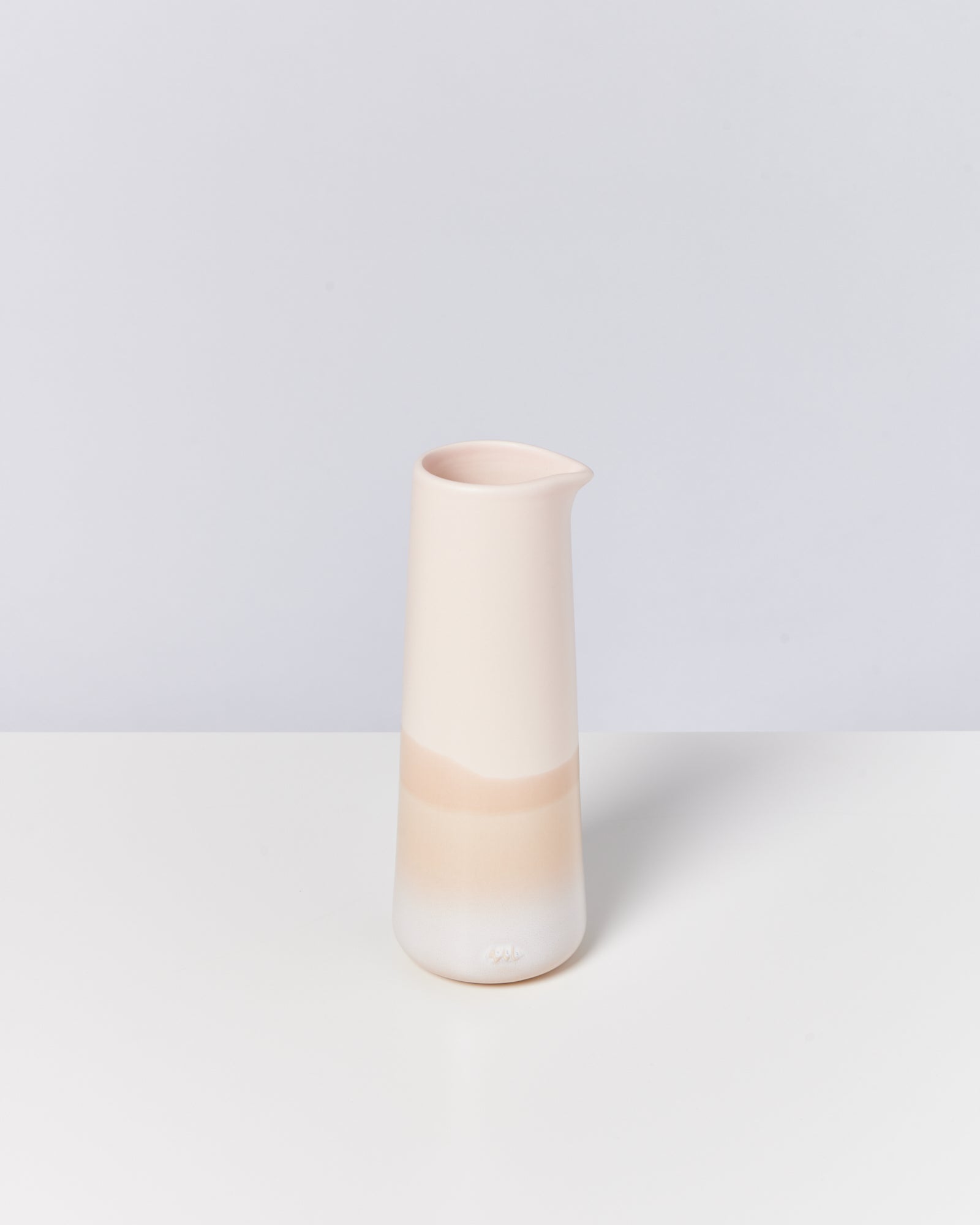 Beiger Keramikkrug mit minimalistischem Design steht auf einer weißen Oberfläche vor einem hellgrauen Hintergrund.