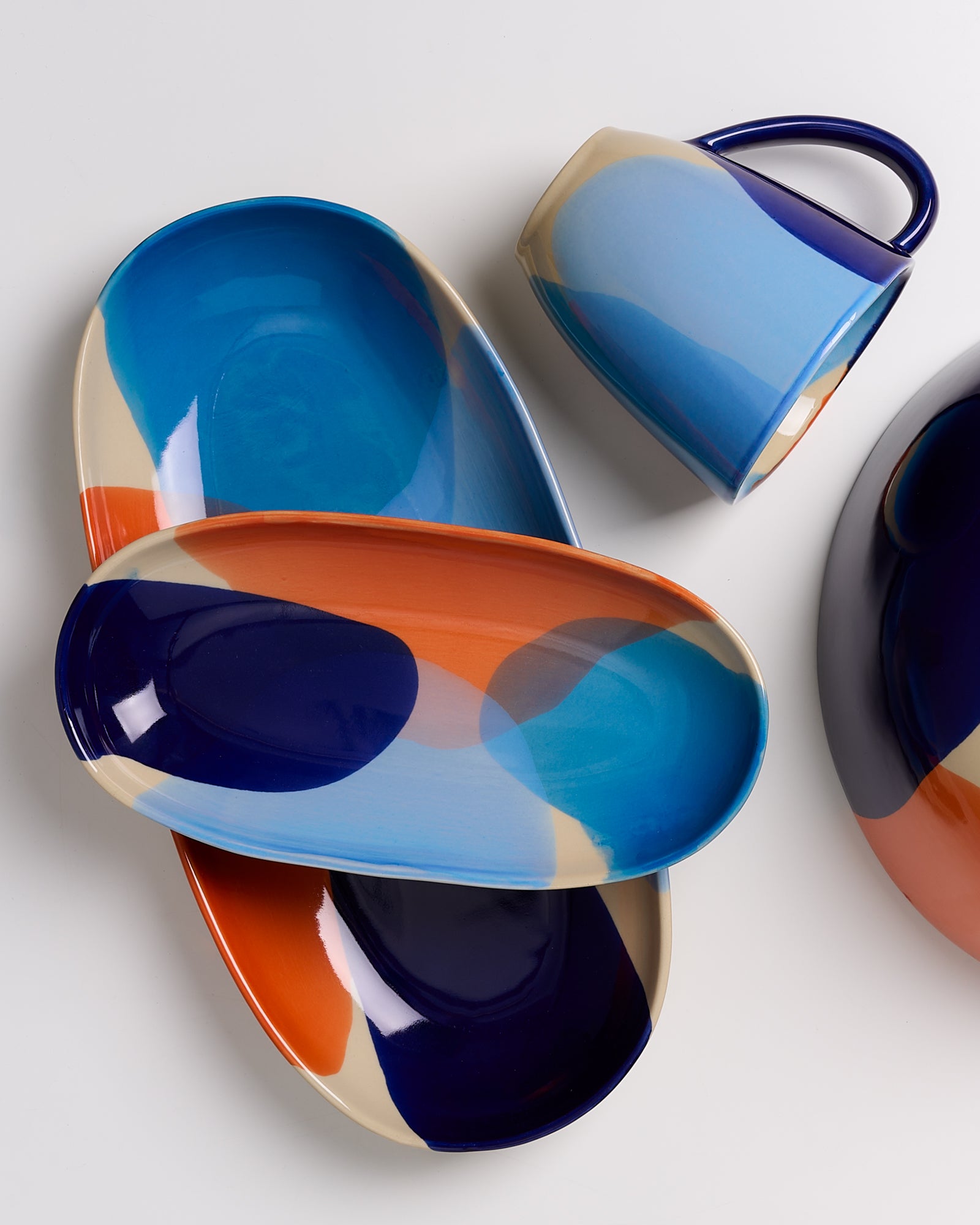 Bunte Teller und Tasse mit abstrakten blauen, orangefarbenen und beigen Mustern auf weißem Hintergrund.