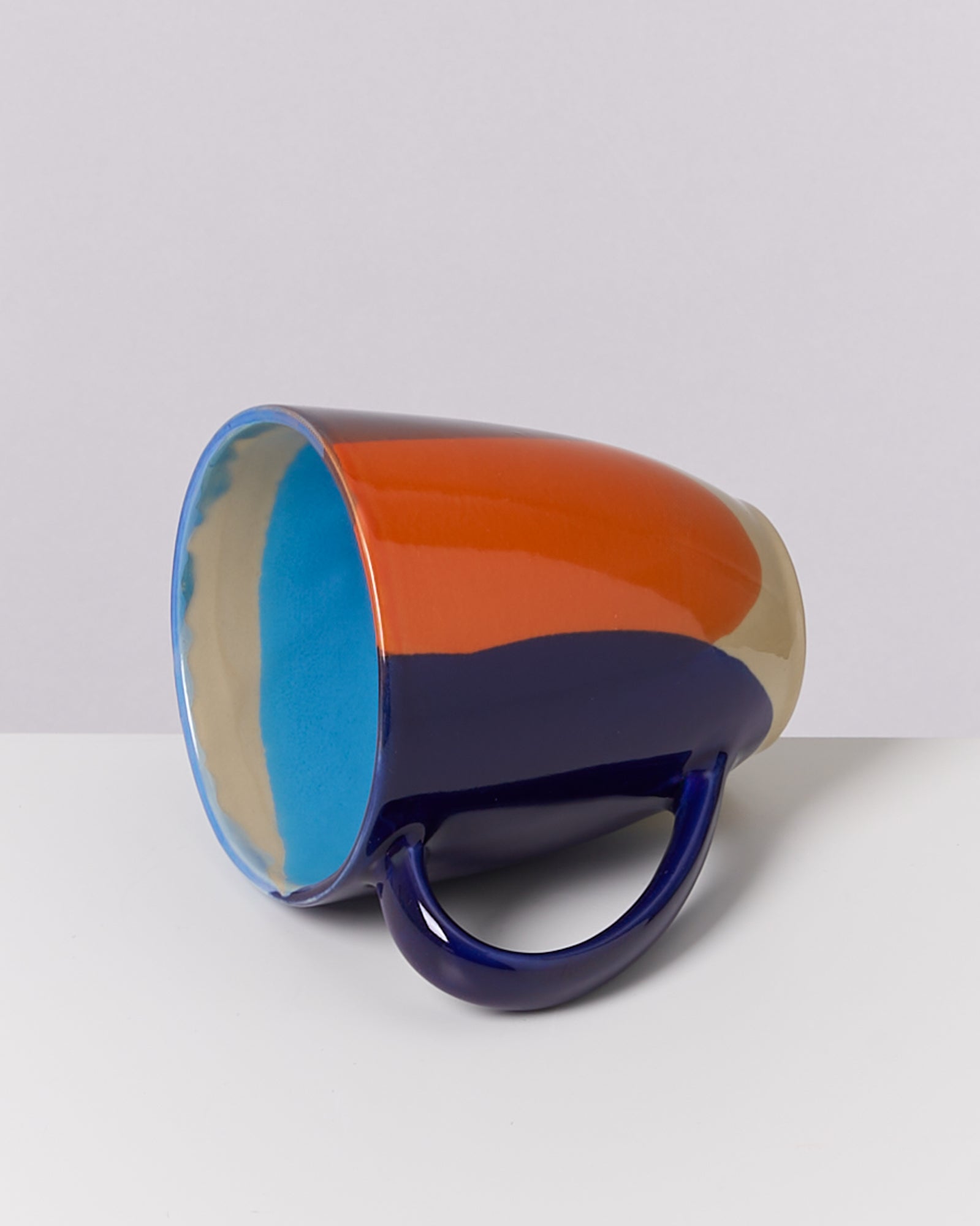 Eine bunt gestreifte Tasse liegt auf der Seite, mit orange, blau und beige Farben im Design.