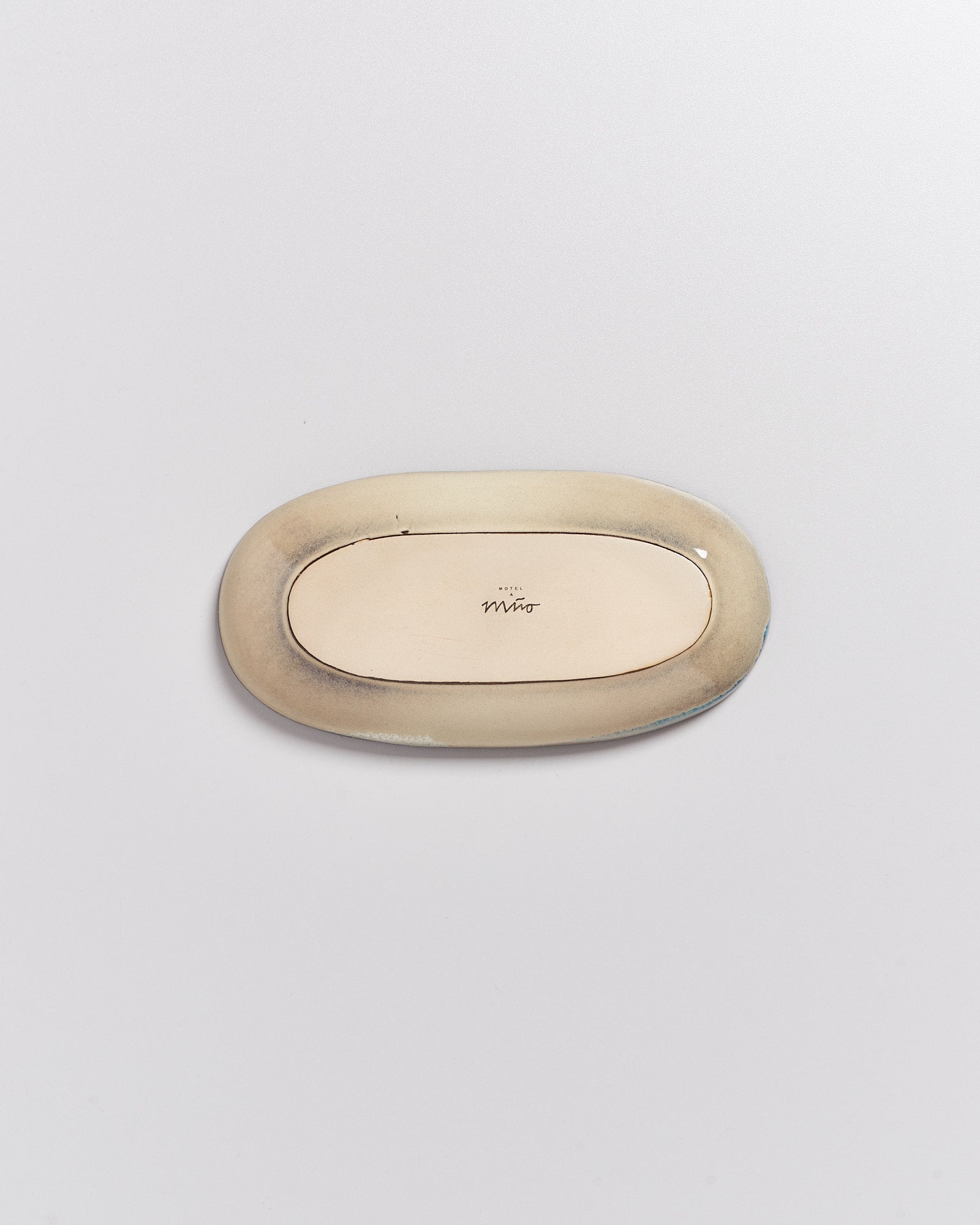 Ovaler, beiger Keramikteller mit einer Unterschrift in der Mitte, auf einer hellen Oberfläche liegend.