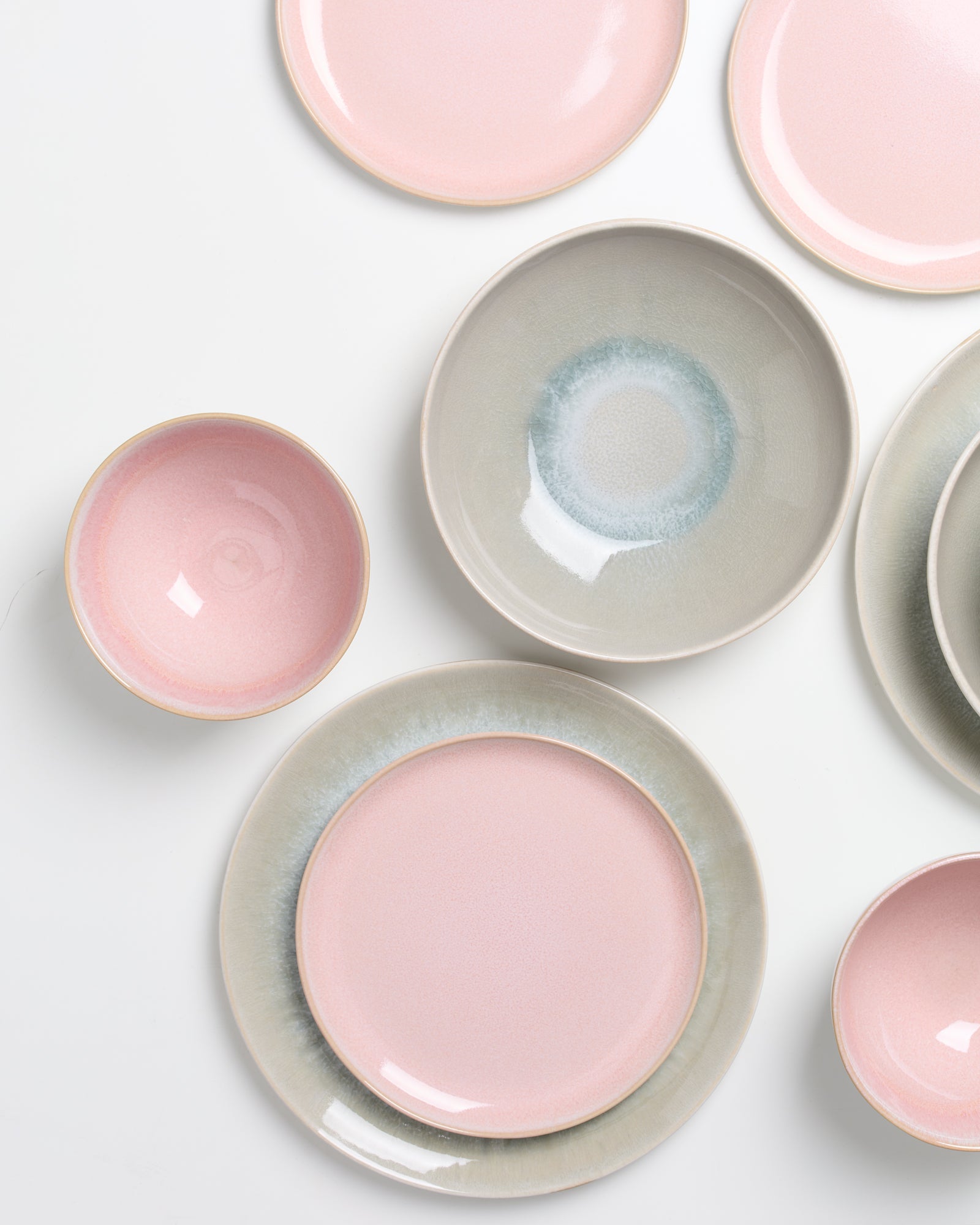 Verschiedene Teller mit rosa und grauen Abstufungen auf weißem Hintergrund angeordnet.
