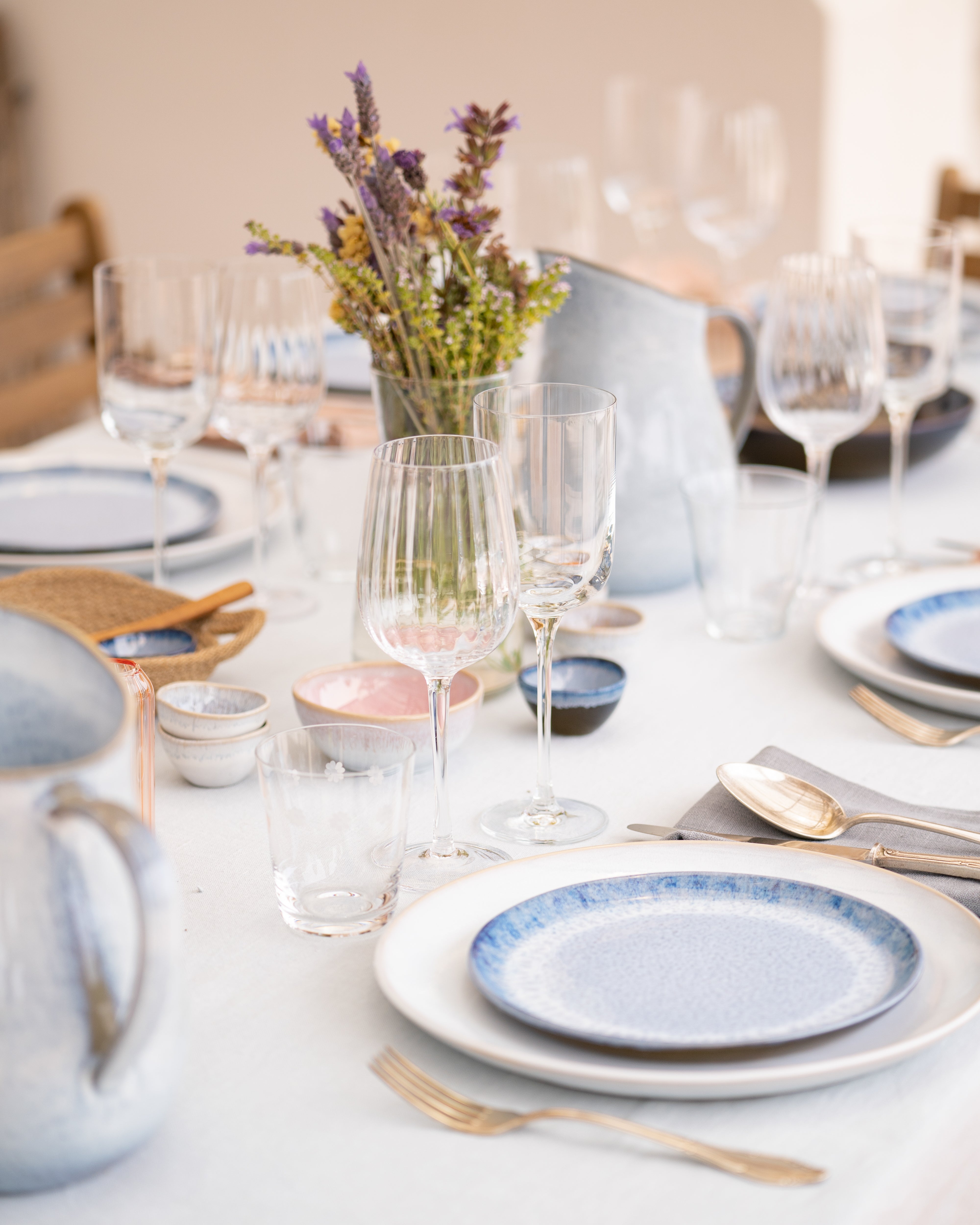 Eleganter Tisch mit blauen Tellern, Gläsern und Blumenarrangement auf weißer Tischdecke.