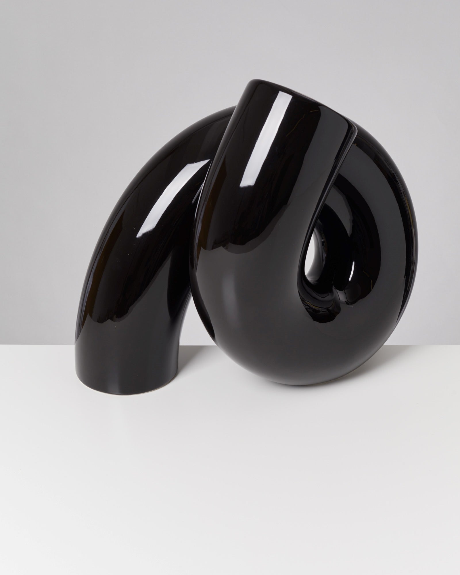 Schwarze, glänzende Skulptur mit geschwungenem, röhrenförmigem Design auf weißem Hintergrund.