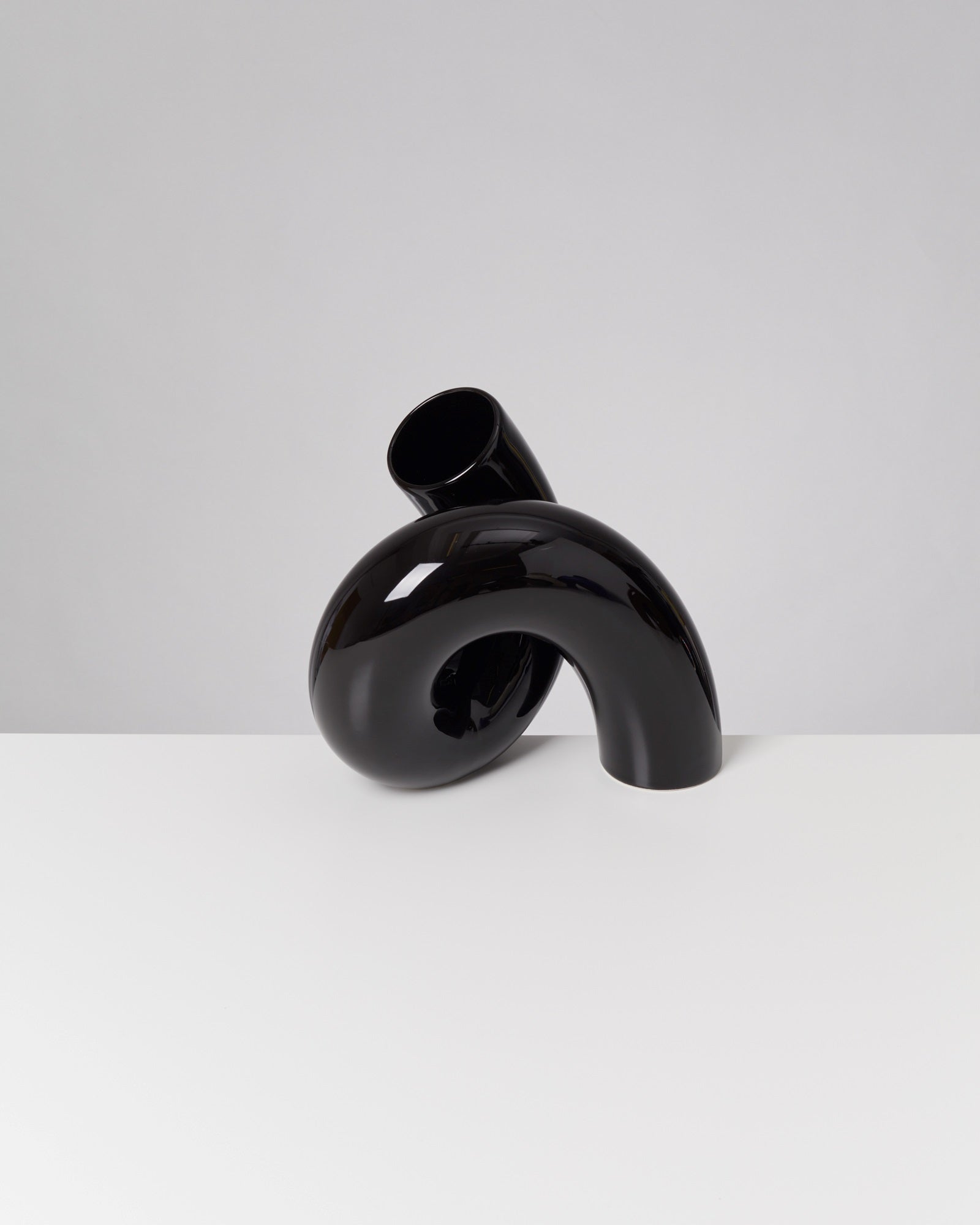 Schwarze, abstrakte Skulptur mit geschwungener Form auf weißem Tisch vor grauem Hintergrund.