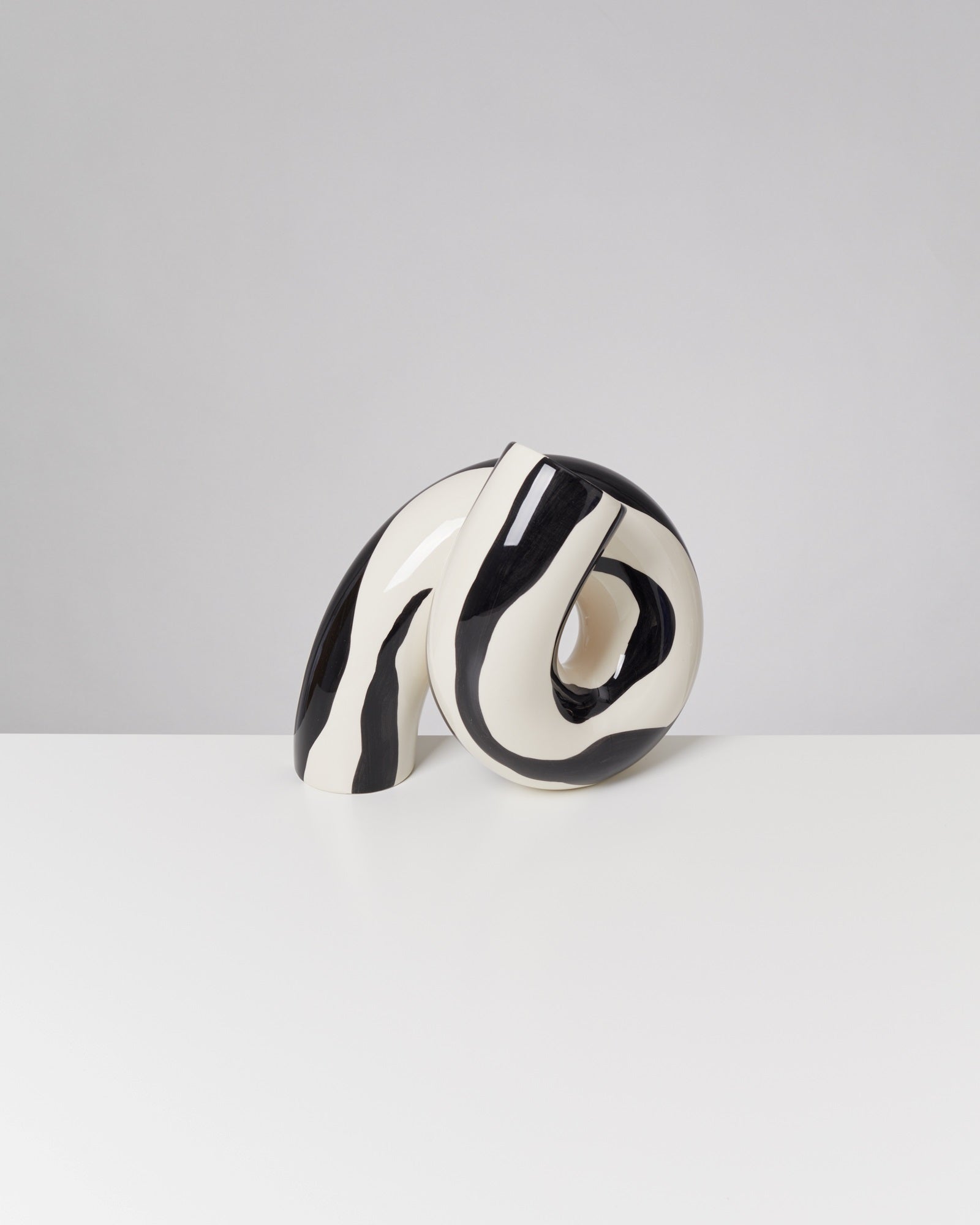 Schwarz-Weiß-gewellte Keramikskulptur auf weißem Tisch vor grauem Hintergrund.
