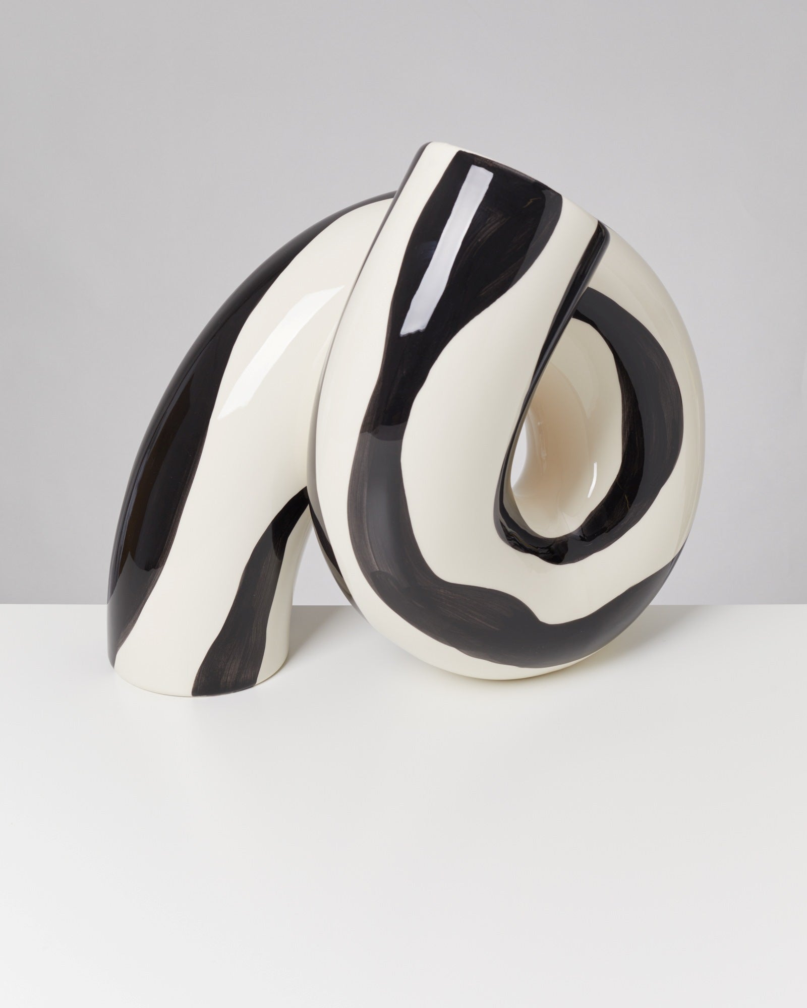 Schwarz-weiß gestreifte Skulptur mit gekrümmter, spiralartiger Form auf weißem Hintergrund.