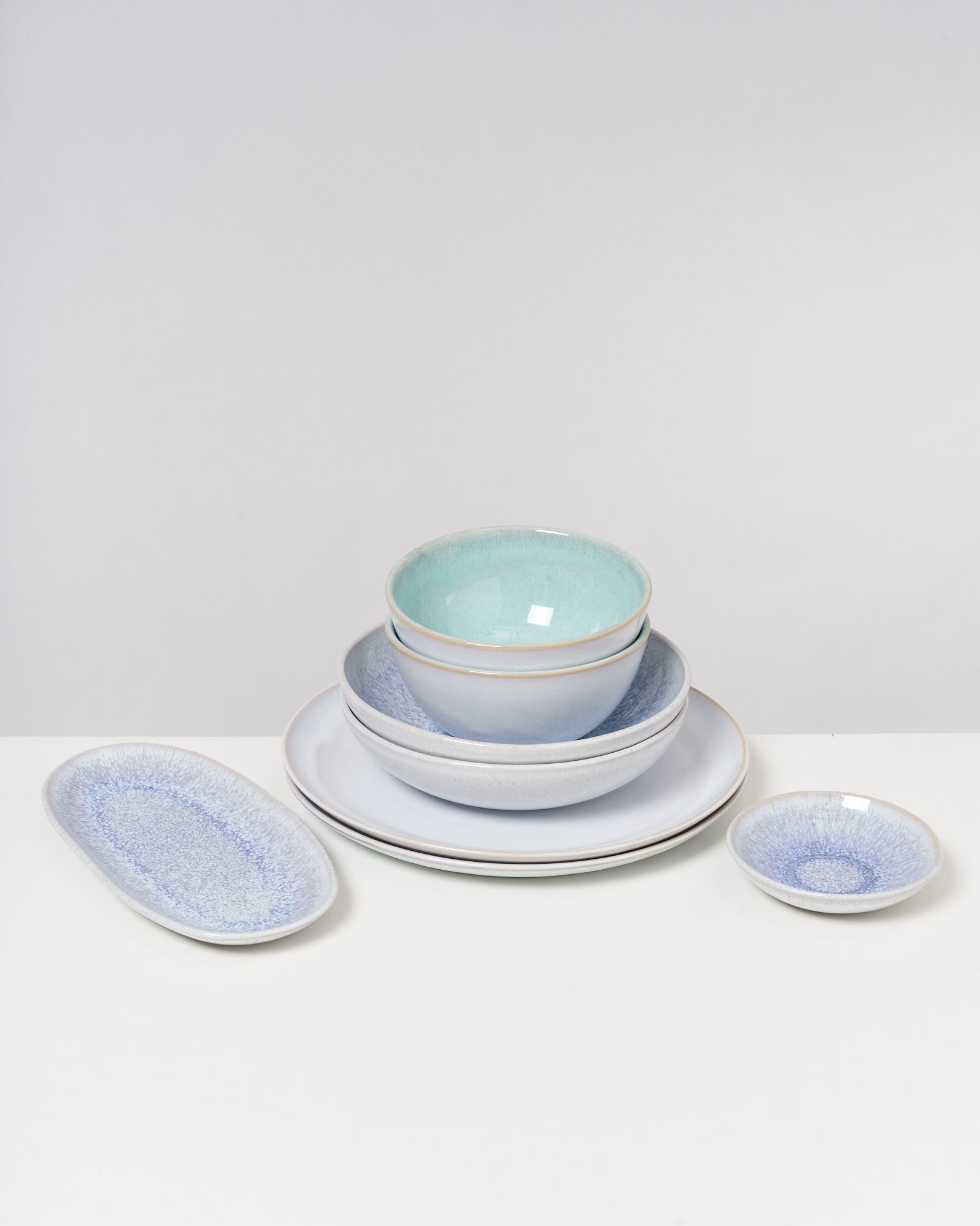 Ein Stapel von Schüsseln und Tellern in verschiedenen Größen und Pastelltönen steht auf einem weißen Tisch.