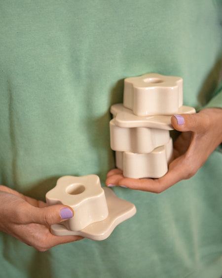 Person hält mehrere cremefarbene, blütenförmige Kerzenhalter in den Händen, mit pastell-lila lackierten Fingernägeln.