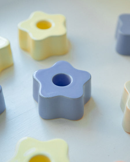 Mehrere sternförmige, pastellfarbene Kerzenhalter liegen auf einer weißen Oberfläche.