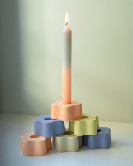 Eine brennende zweifarbige Kerze steht in einem pastellfarbenen, sternförmigen Kerzenhalter-Stapel.