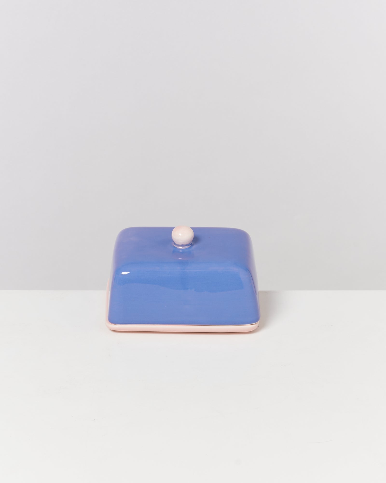 Quadratische blaue Butterdose mit knopfförmigem Griff auf weißem Hintergrund.