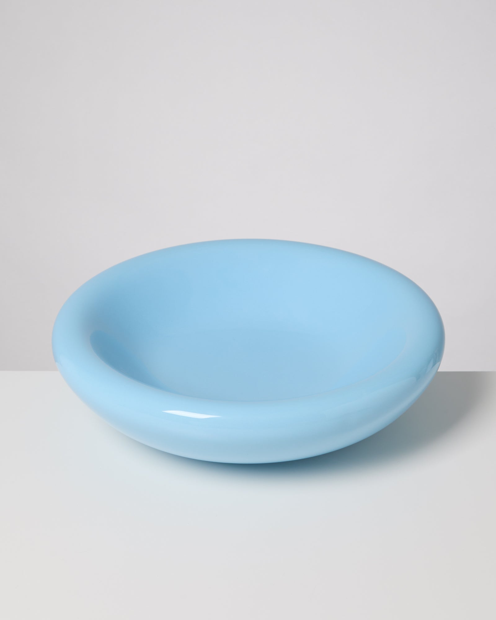 Hellblaue, runde Schüssel mit glatter Oberfläche auf einem hellen Tisch vor grauem Hintergrund.