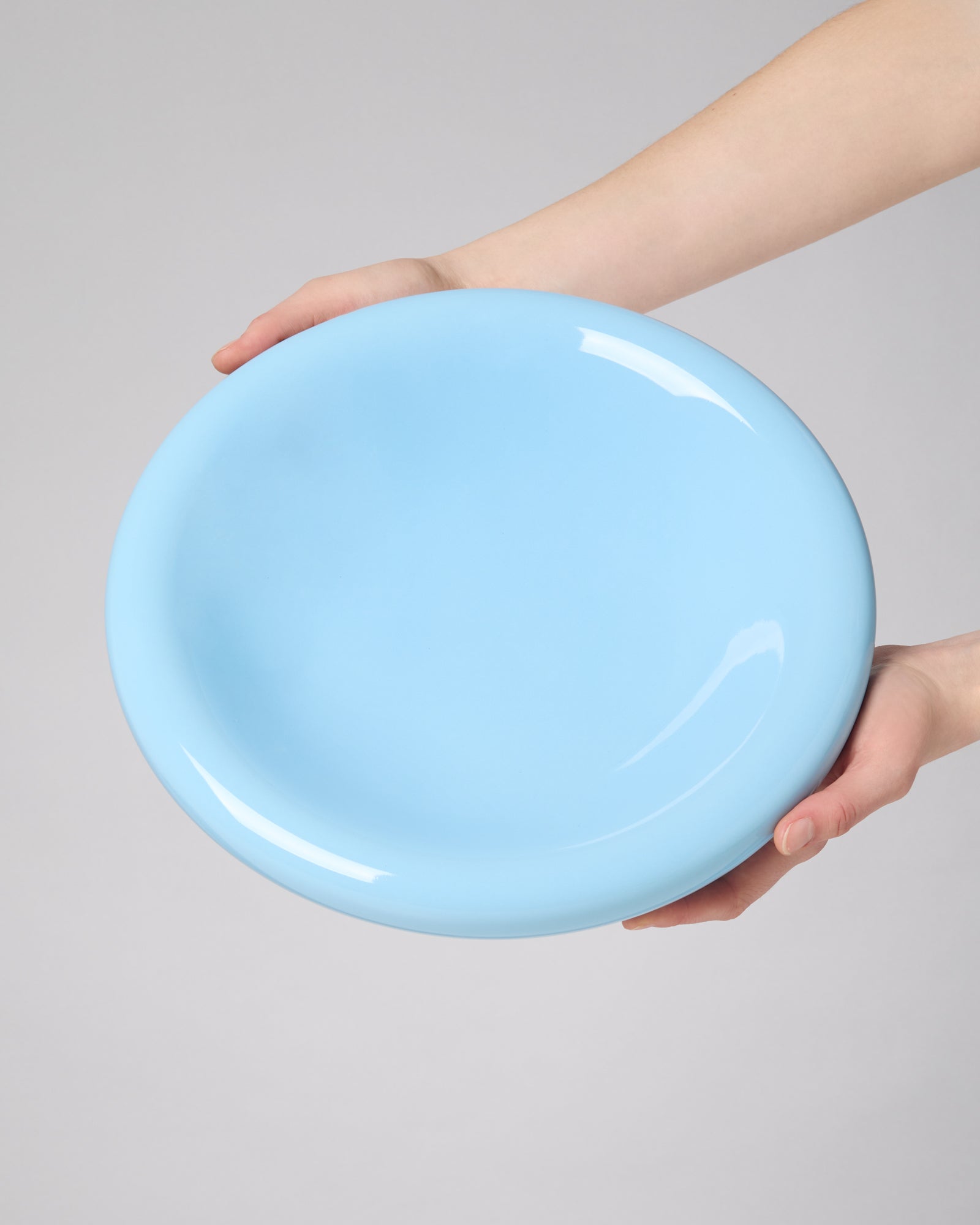 Hände halten einen hellblauen Teller vor einem neutralen Hintergrund.
