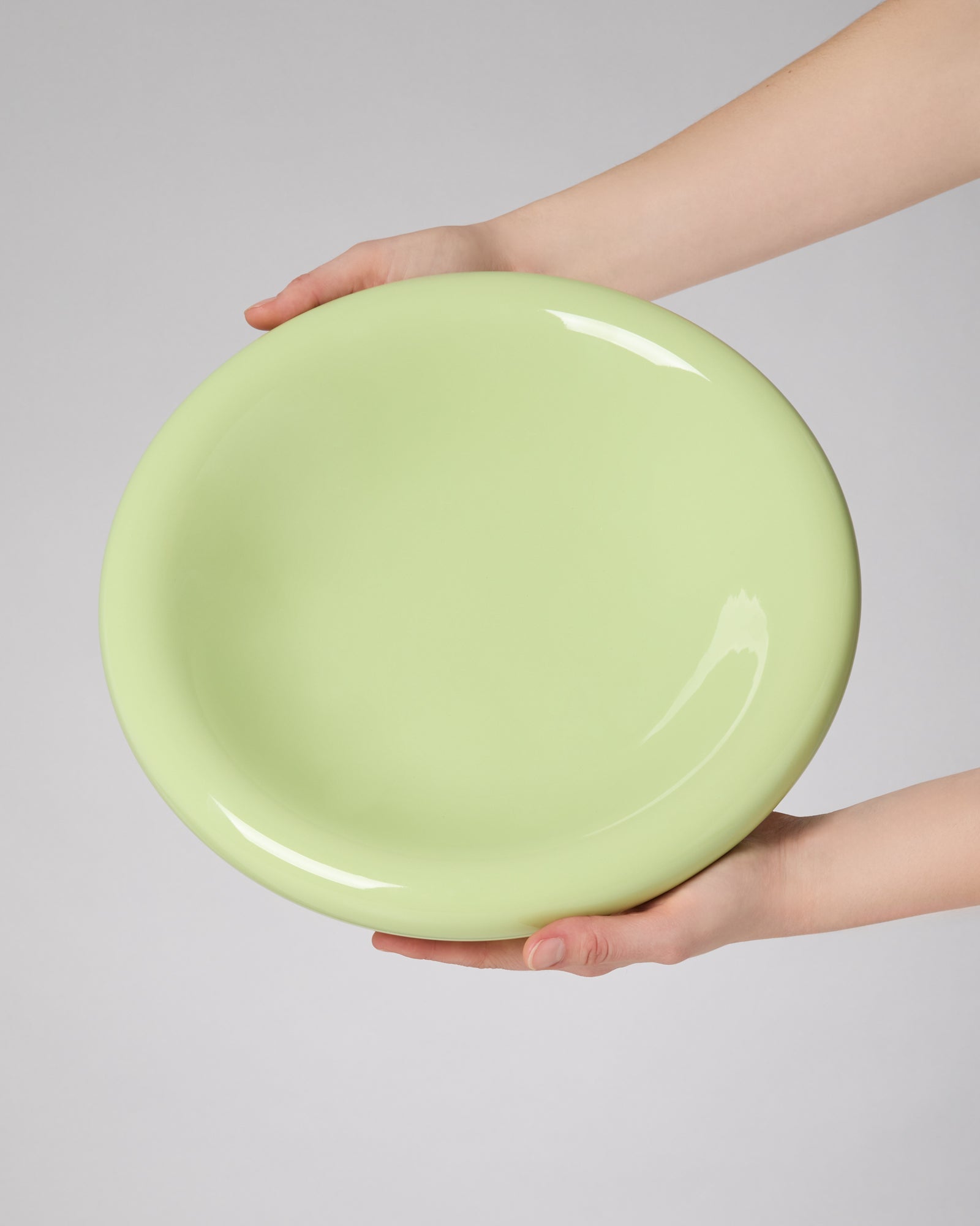 Zwei Hände halten einen großen, hellgrünen Teller vor einem grauen Hintergrund.