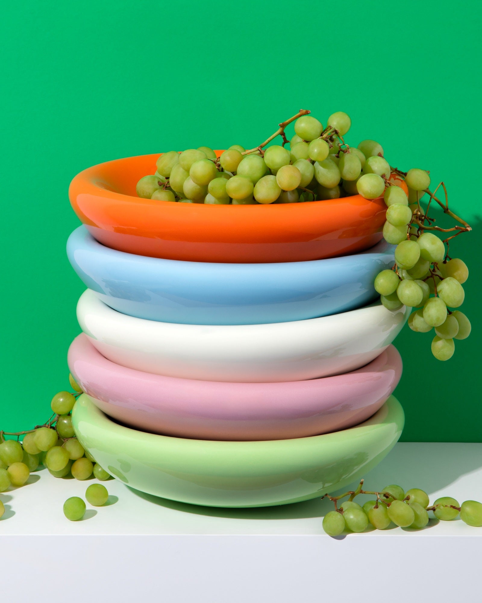 Ein Stapel bunter Schalen mit grünen Trauben darauf und einem grünen Hintergrund.