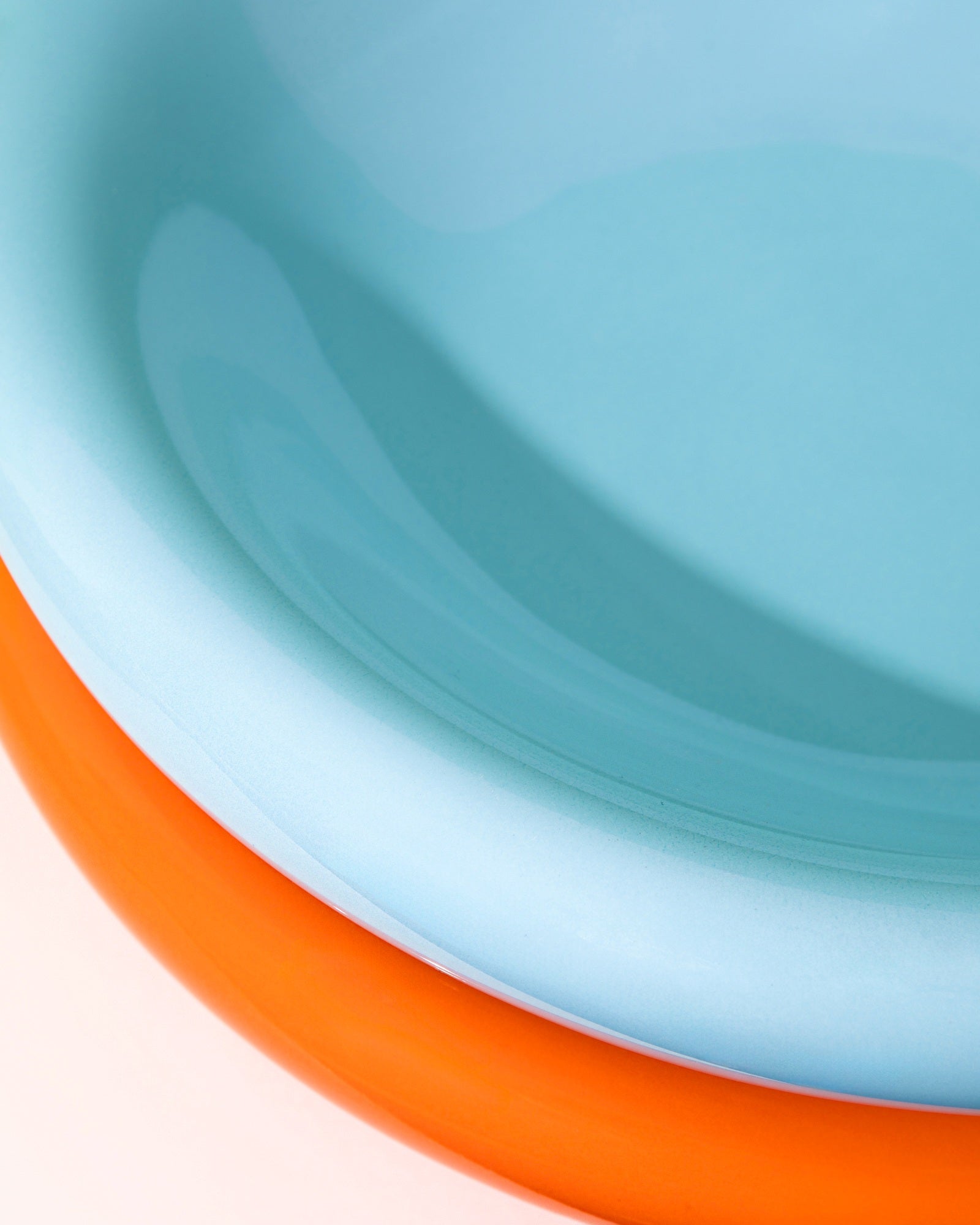 Nahaufnahme von zwei gestapelten Tellern, oben hellblau und unten orange.