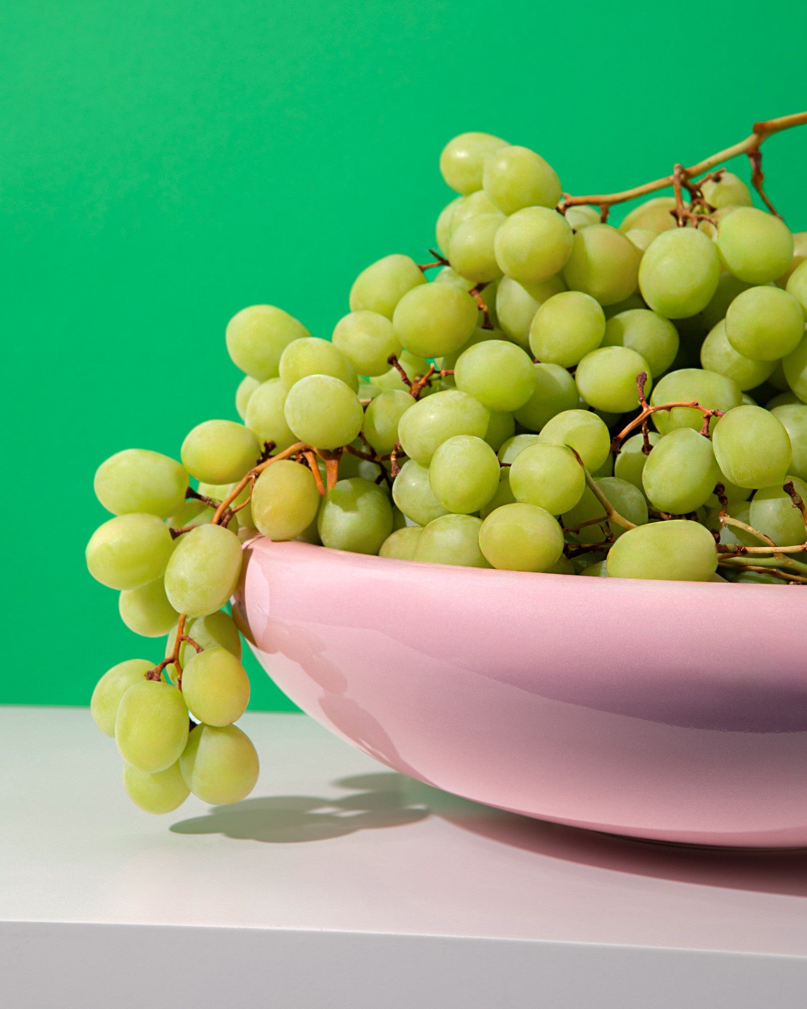 Grüne Weintrauben in einer rosa Schüssel vor grünem Hintergrund.