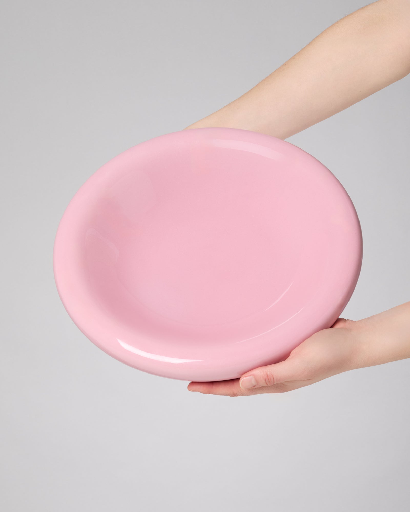 Zwei Hände halten eine große rosafarbene Schüssel vor neutralem Hintergrund.