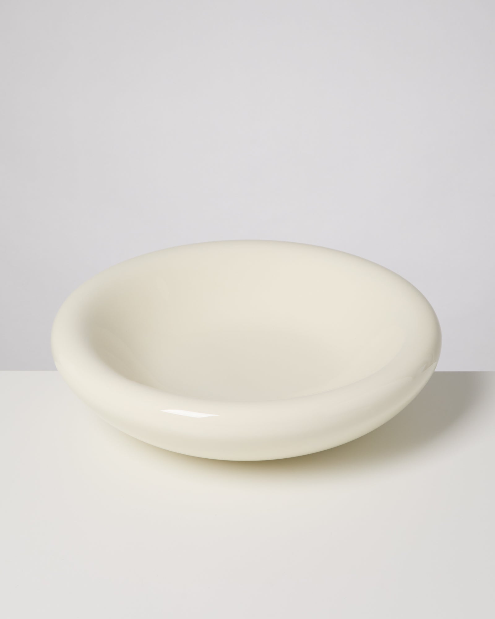 Beiger, glänzender Keramikstuhl mit abgerundeter Form auf einer weißen Fläche fotografiert.