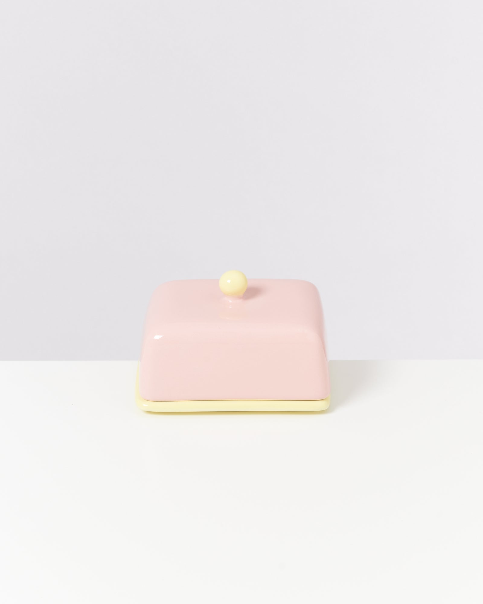 Rosa Butterdose mit gelbem Knauf und Boden auf weißem Hintergrund.