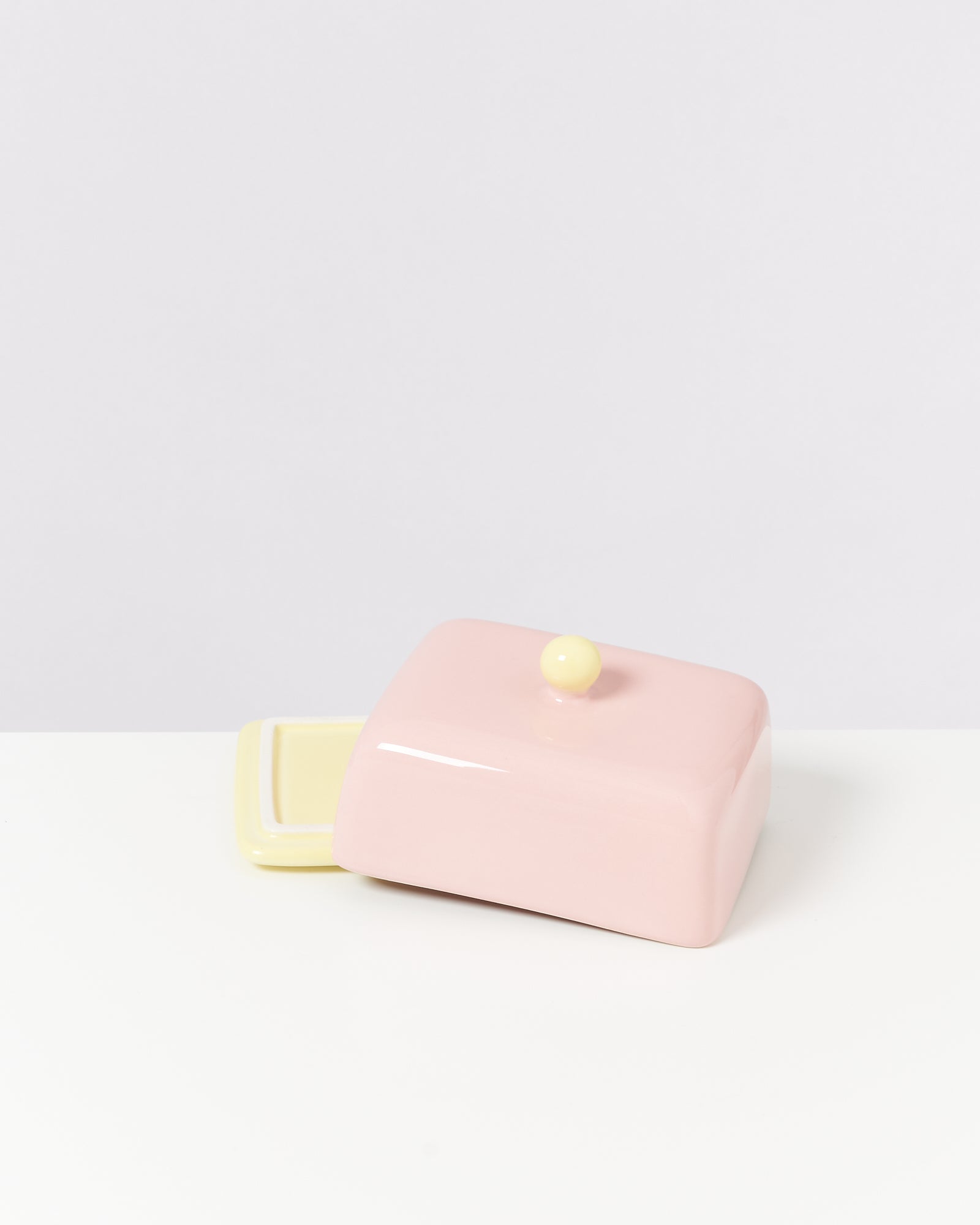 Rosafarbene Butterdose mit gelbem Deckelknauf auf einem weißen Hintergrund.