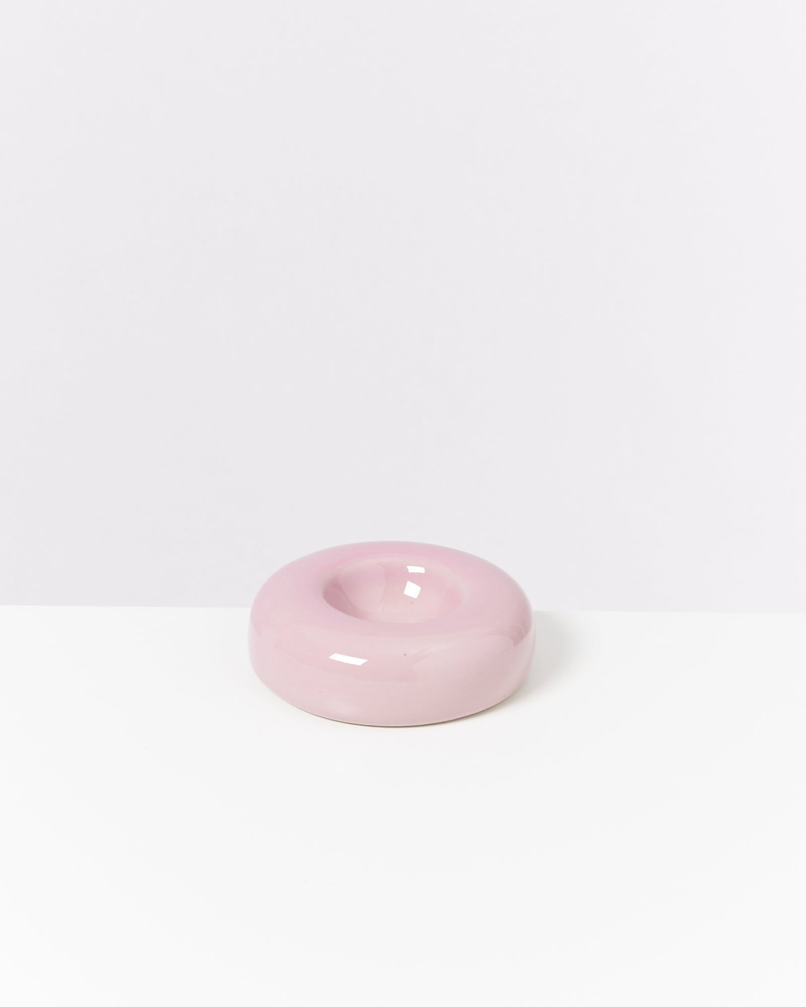 Rosa, glänzende keramikartige Skulptur in Form eines Donuts auf einem weißen Hintergrund.