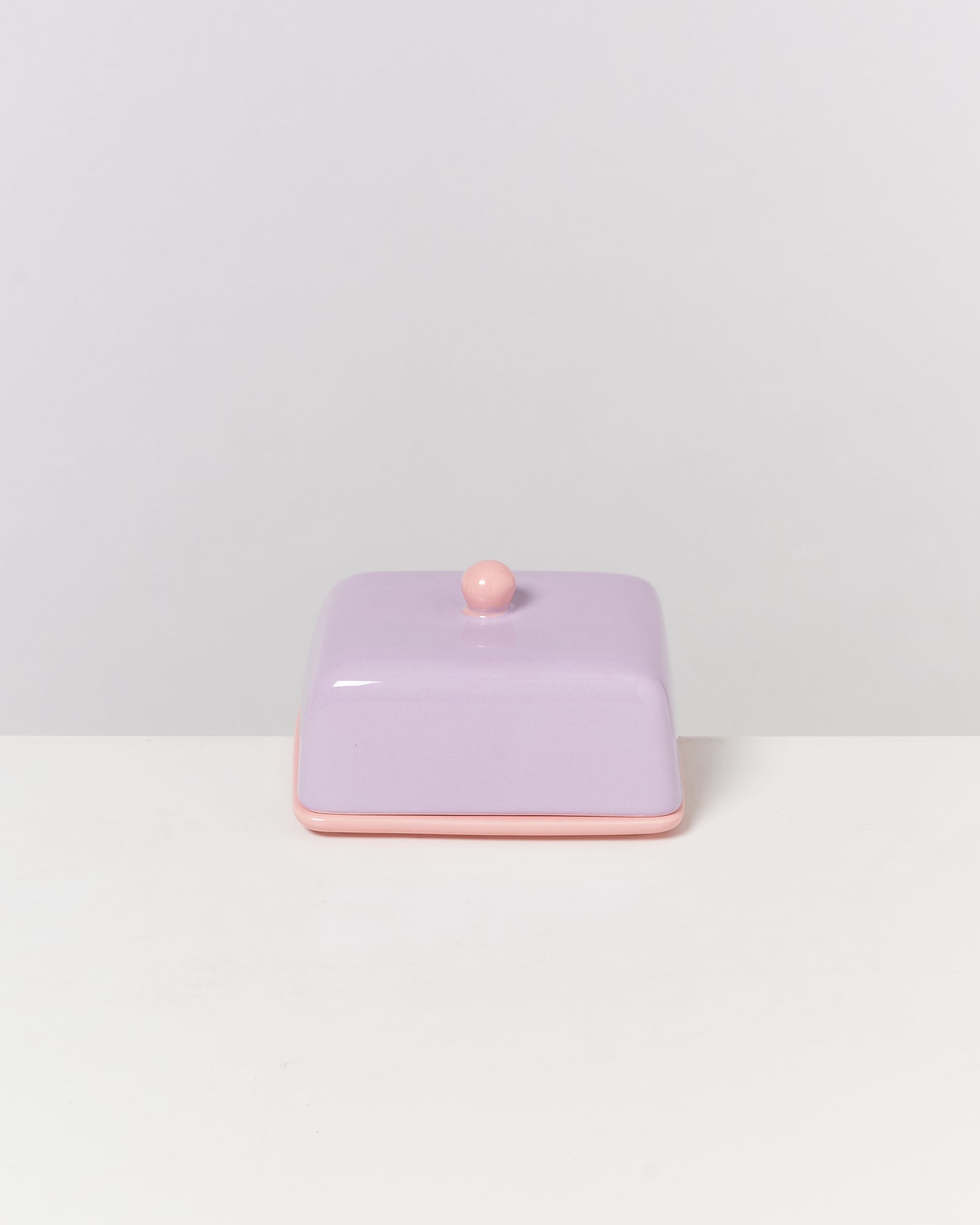 Lila Butterdose mit rosa Rand und Knauf auf weißem Hintergrund.