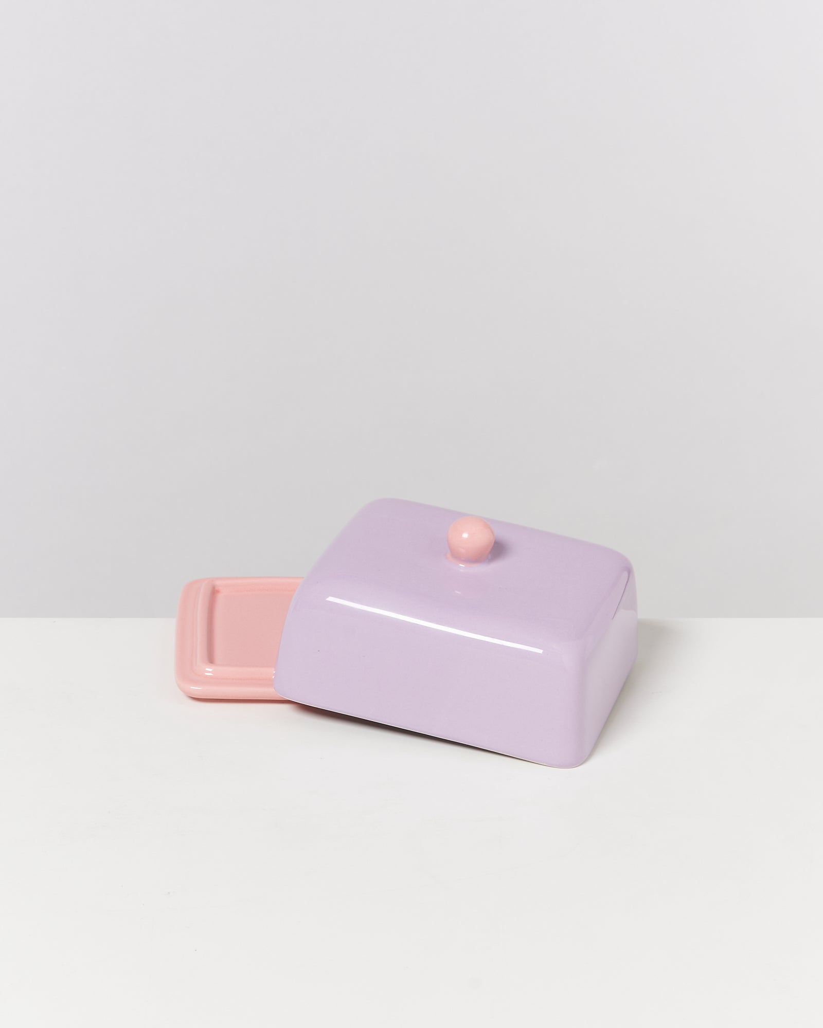 Eine lila Butterdose mit rosa Griff und Boden auf einem weißen Hintergrund.