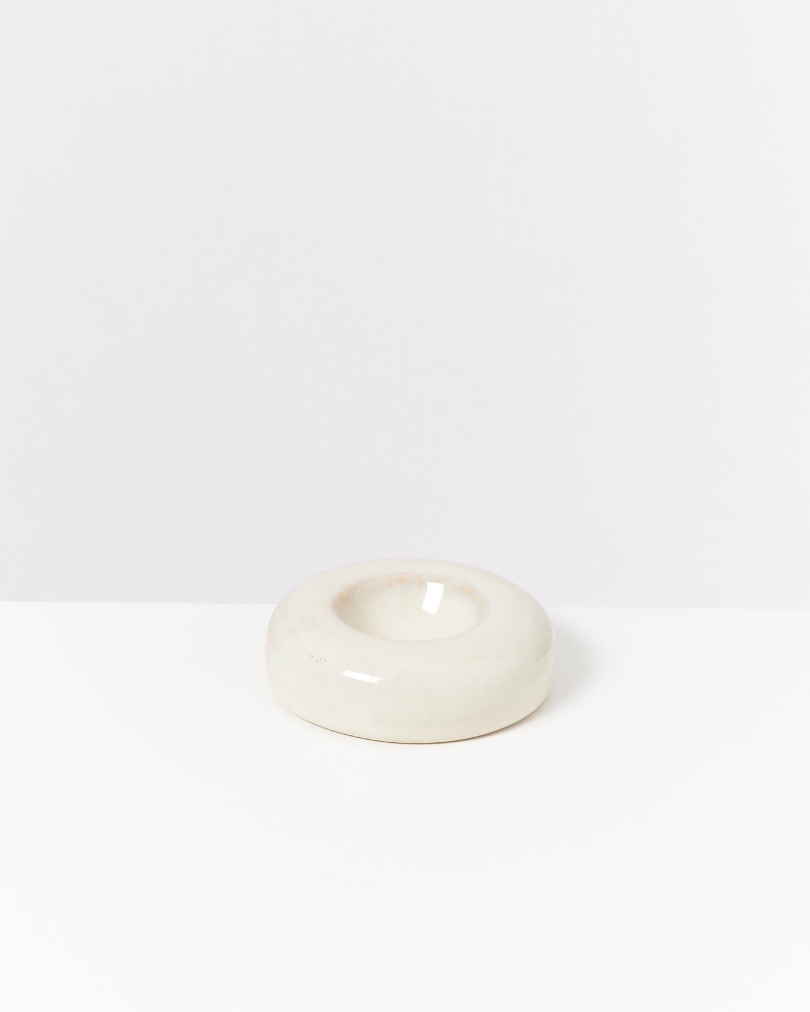 Beiger, runder Kerzenhalter mit einer glänzenden Oberfläche auf weißem Hintergrund.