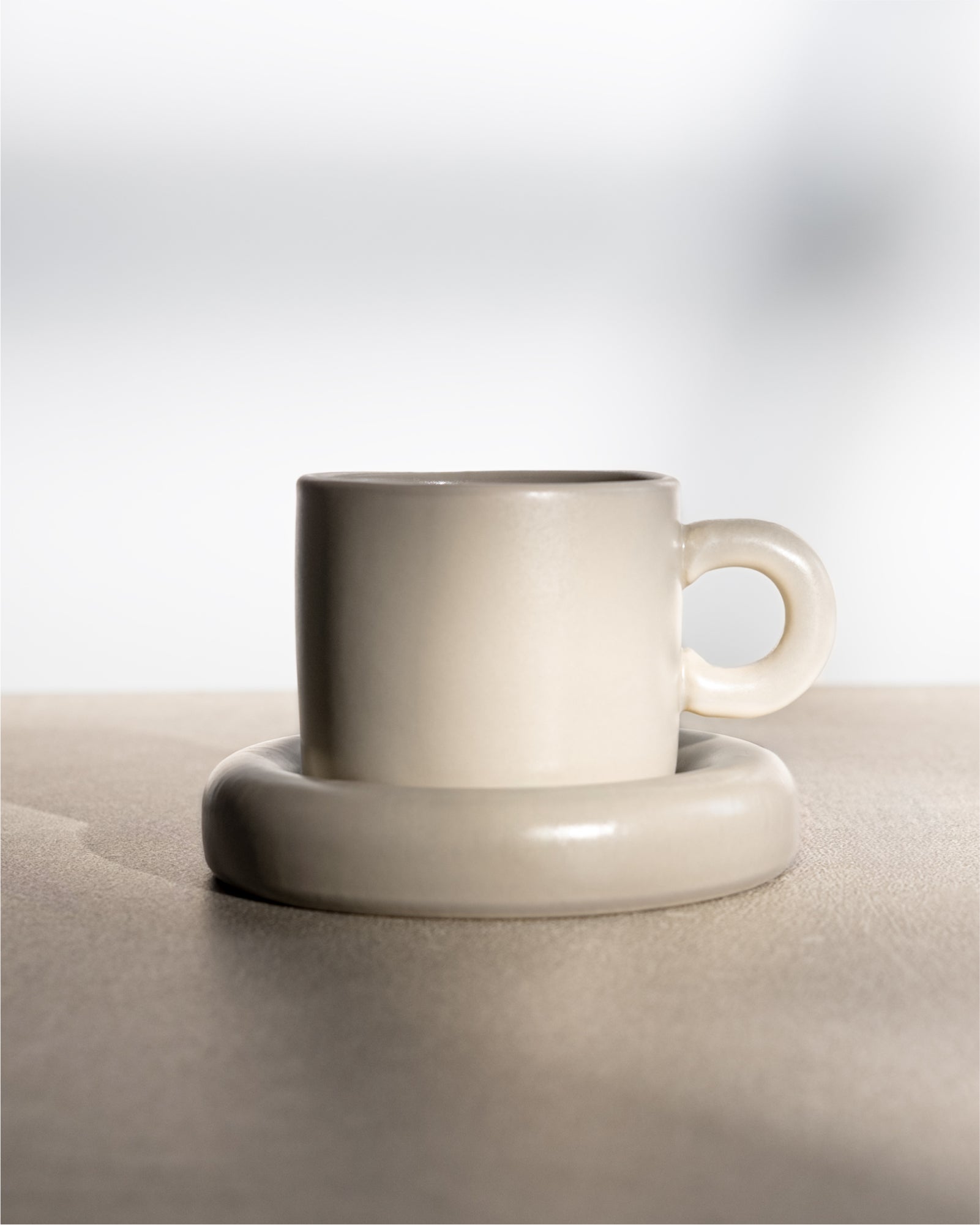 Weiße Keramiktasse mit passender Untertasse auf einer hellen Oberfläche.