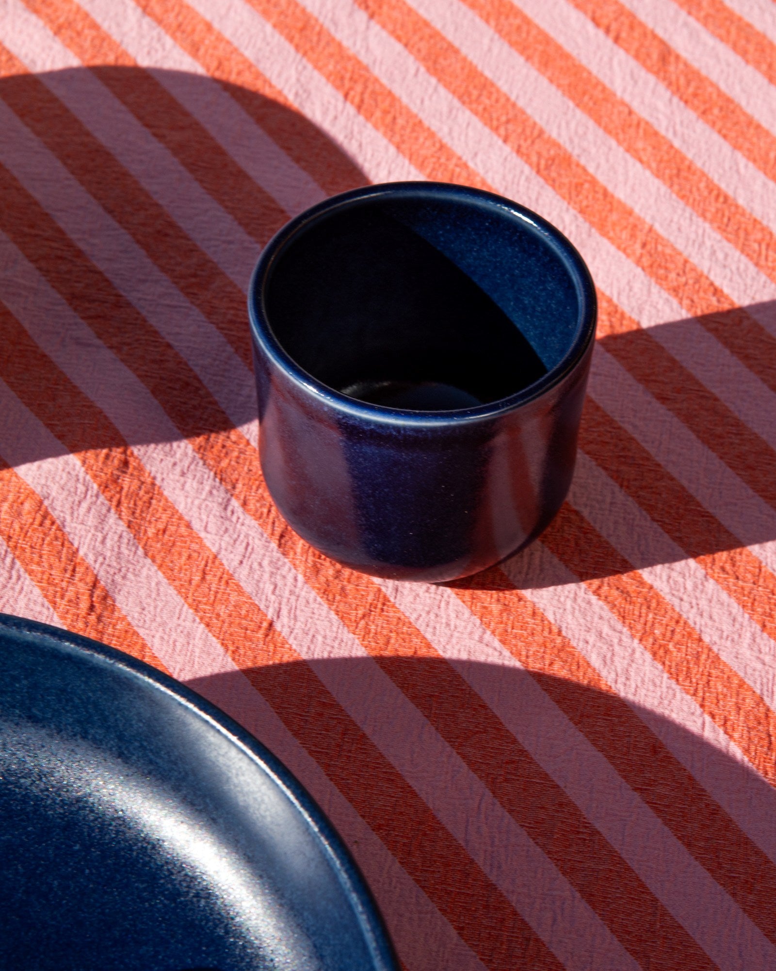 Dunkelblaue Tasse und Teller auf gestreifter rosa-orangefarbener Tischdecke.