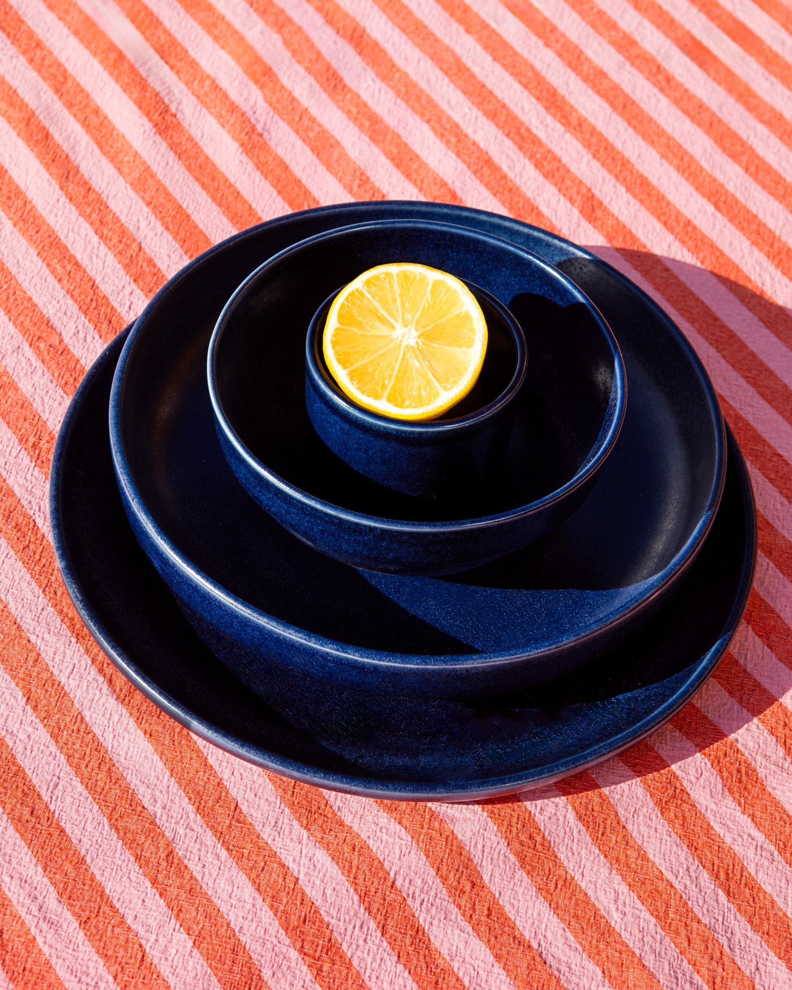 Gestapelte schwarze Teller mit einer Zitronenscheibe darauf liegen auf einem gestreiften, pink-orangefarbenen Tuch.