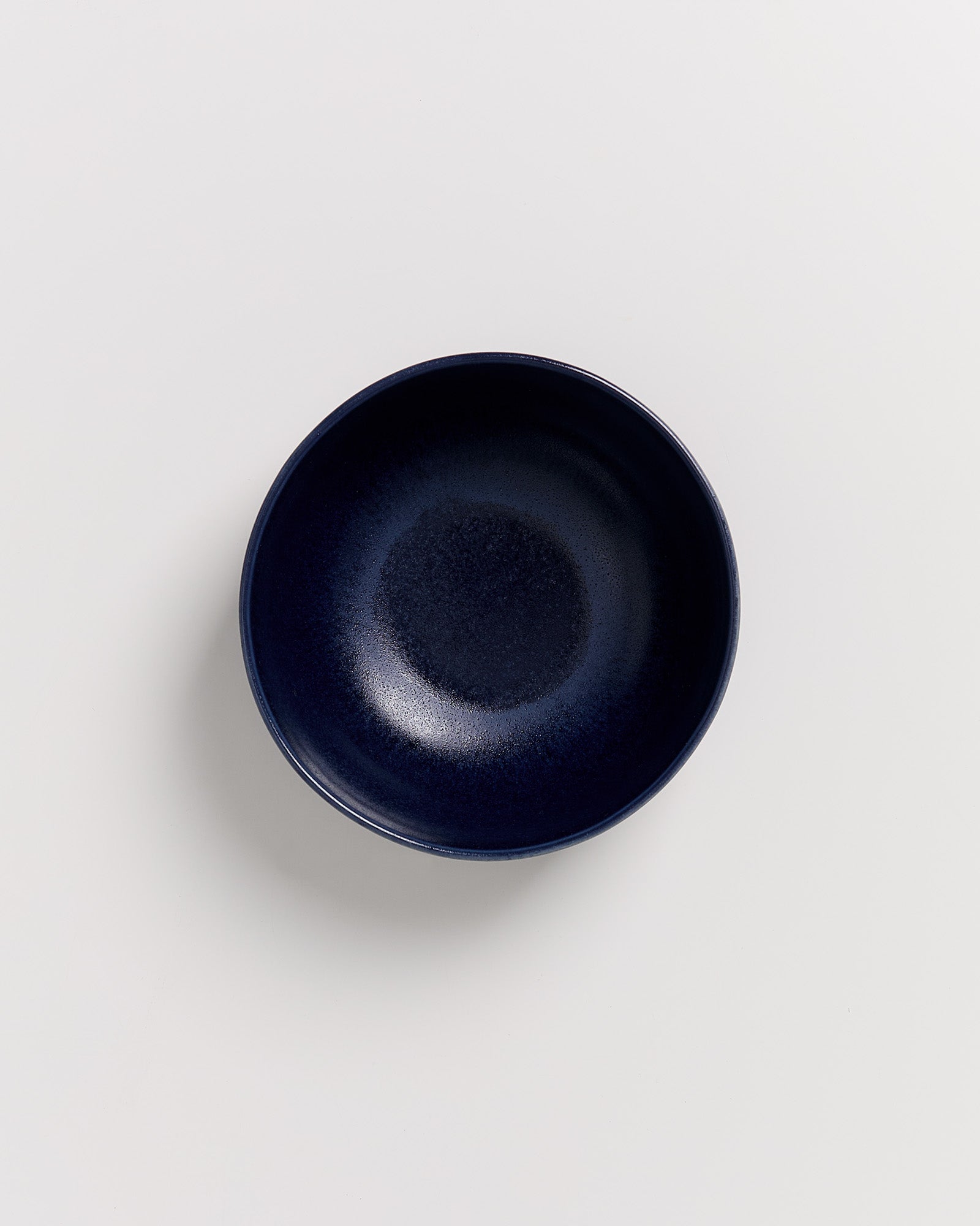 Dunkelblaue Schüssel aus Keramik auf weißem Hintergrund, von oben betrachtet.