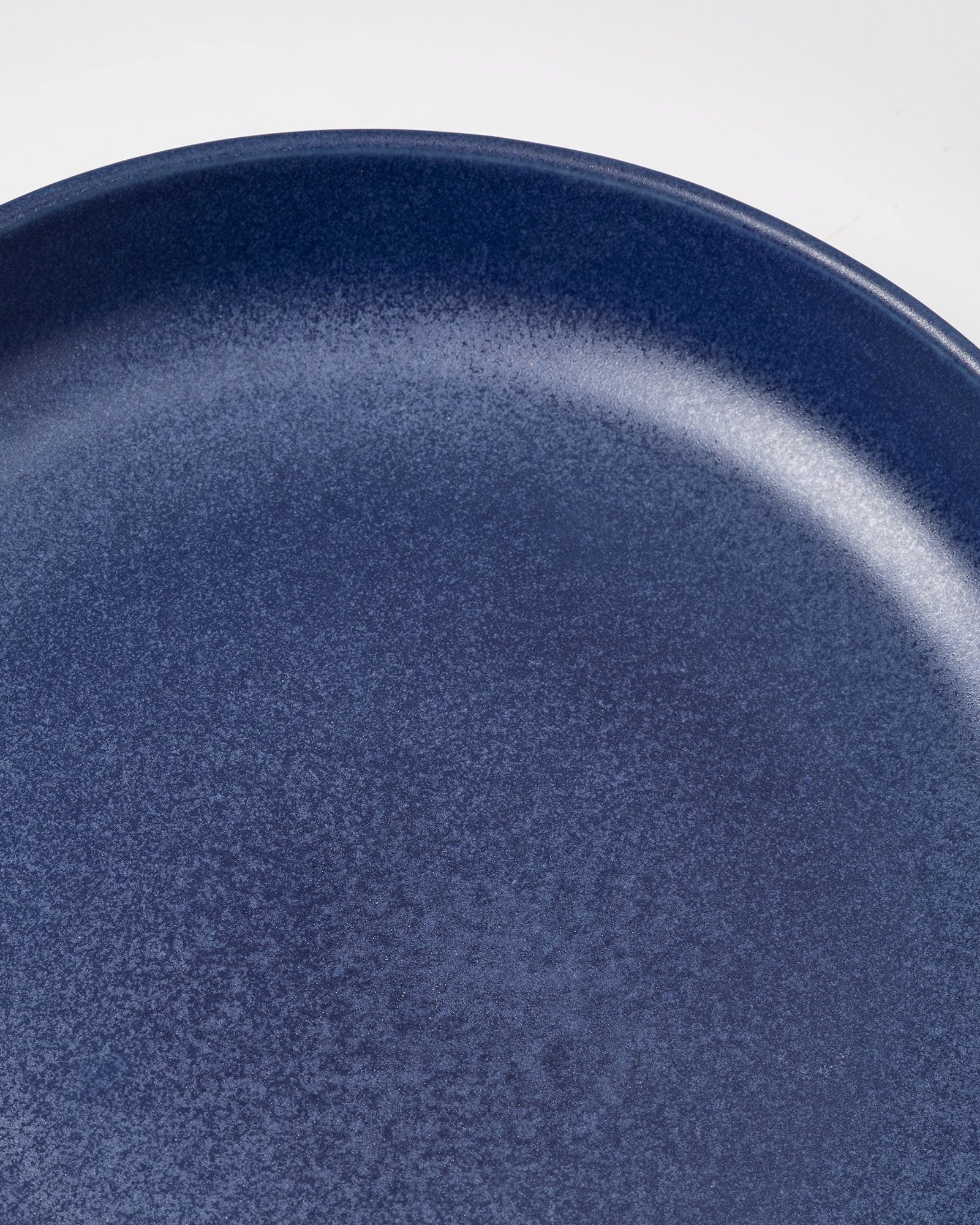 Nahaufnahme eines dunkelblauen Tellers mit gesprenkelter Oberfläche vor weißem Hintergrund.