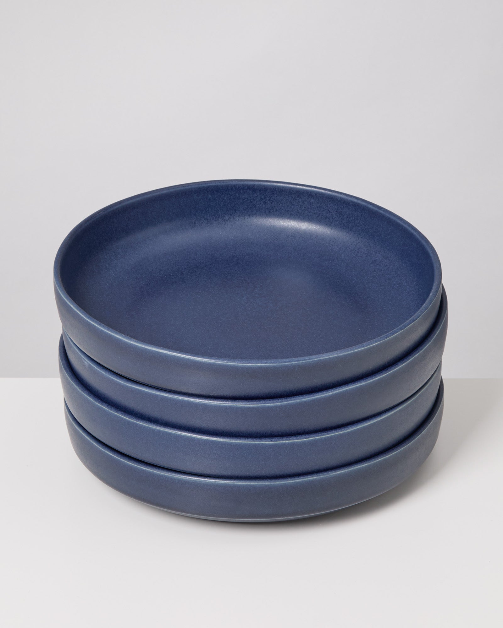 Vier gestapelte dunkelblaue Teller auf einem weißen Hintergrund.