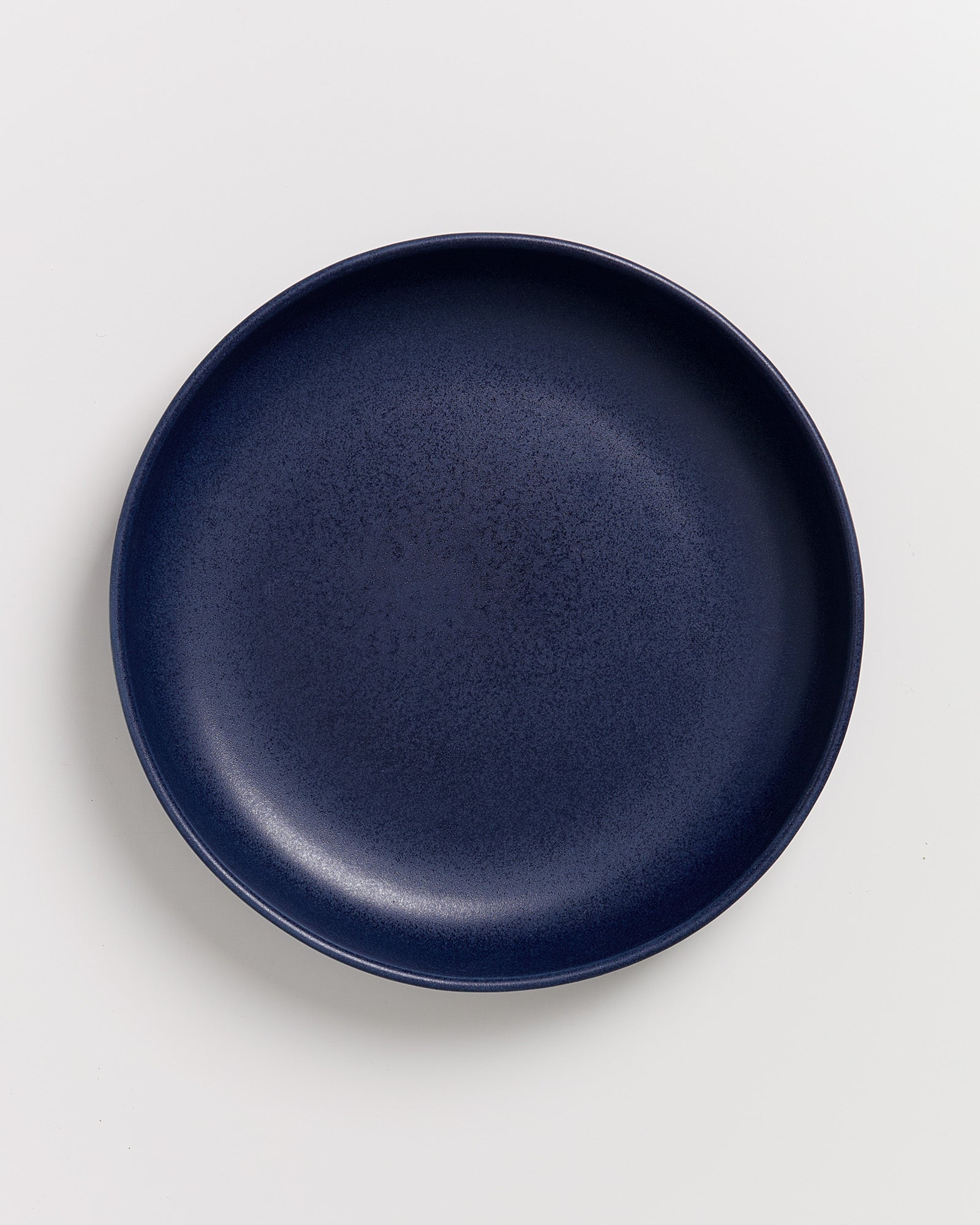 Dunkelblauer Teller auf weißem Hintergrund, von oben betrachtet.