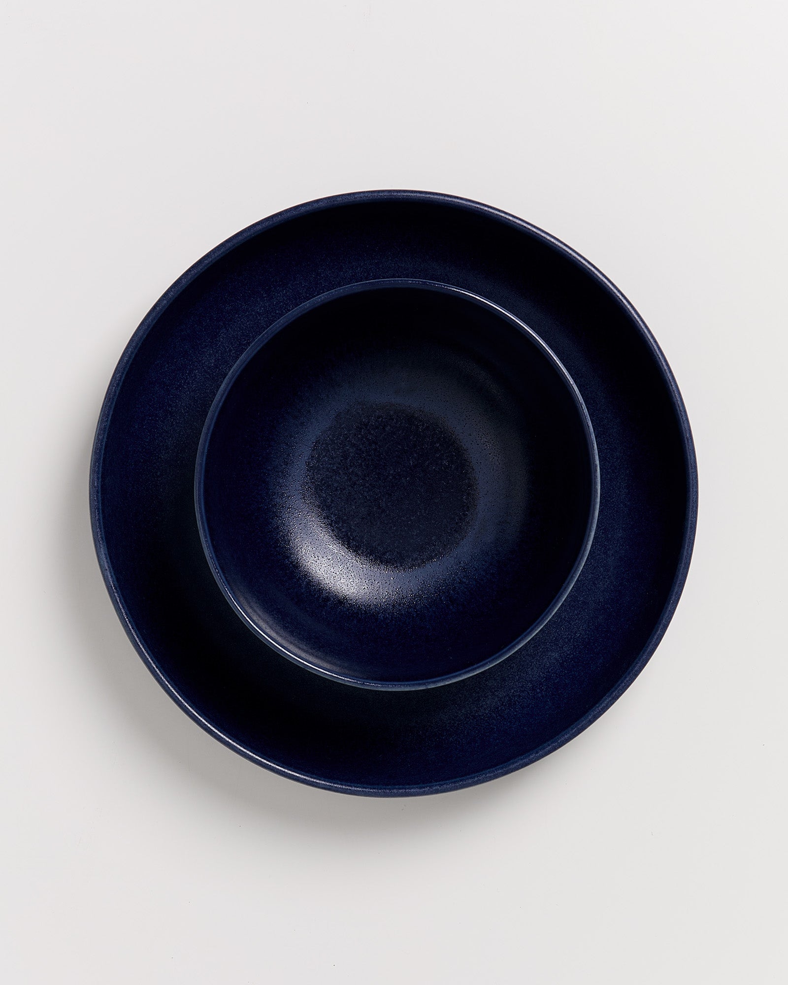 Zwei ineinander gestapelte dunkelblaue Teller auf einem weißen Hintergrund.