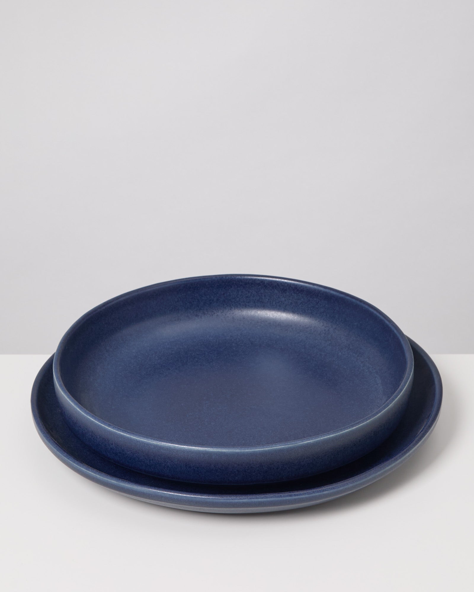 Zwei blaue Teller, übereinandergestapelt, auf einer weißen Oberfläche.