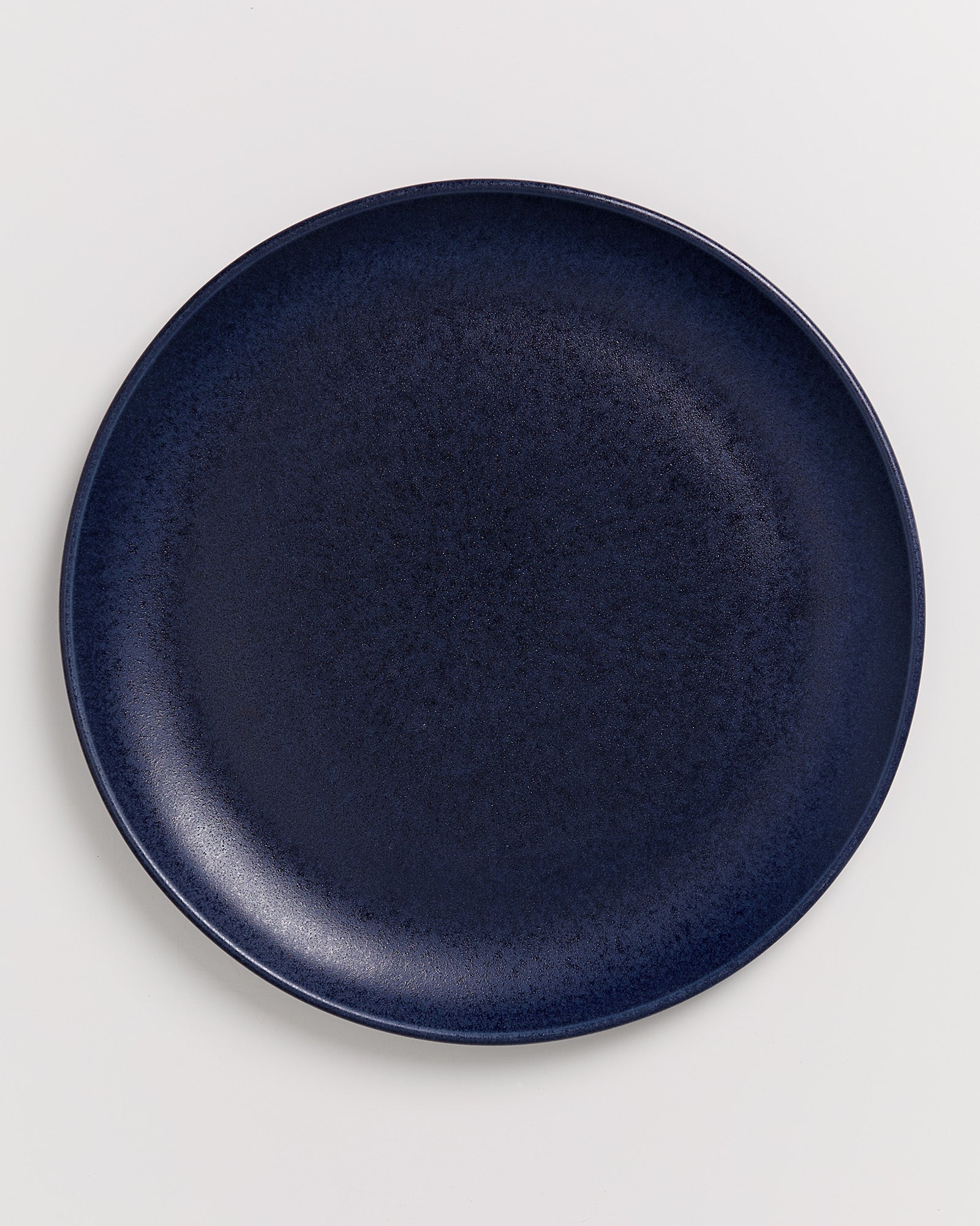 Dunkelblauer, runder Teller auf weißem Hintergrund.