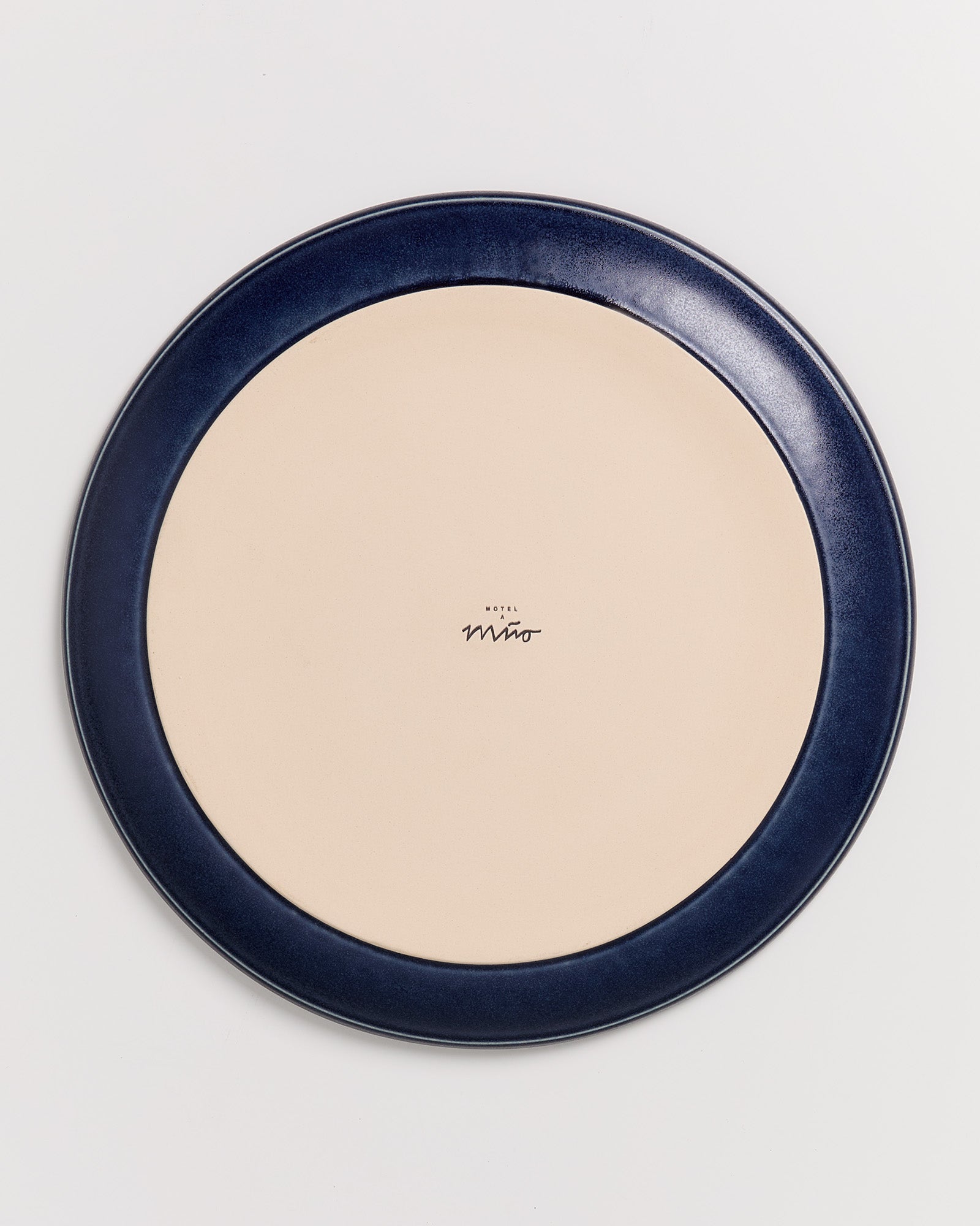 Runder Teller mit dunkelblauem Rand und beigem Mittelteil, darauf steht "Hotel Miró".