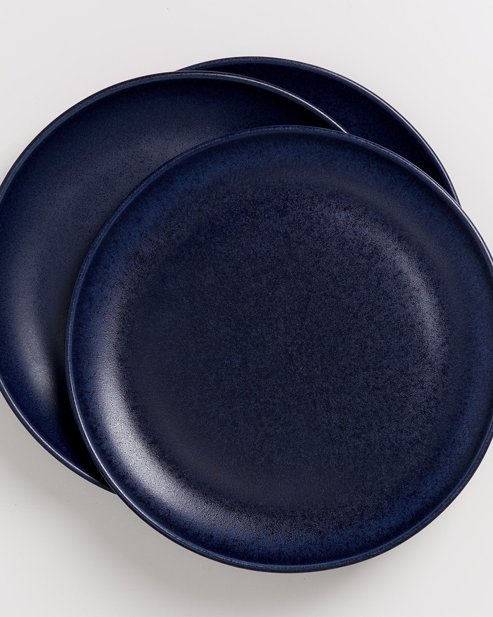 Zwei übereinander gelegte, dunkelblaue Teller auf einem weißen Hintergrund.