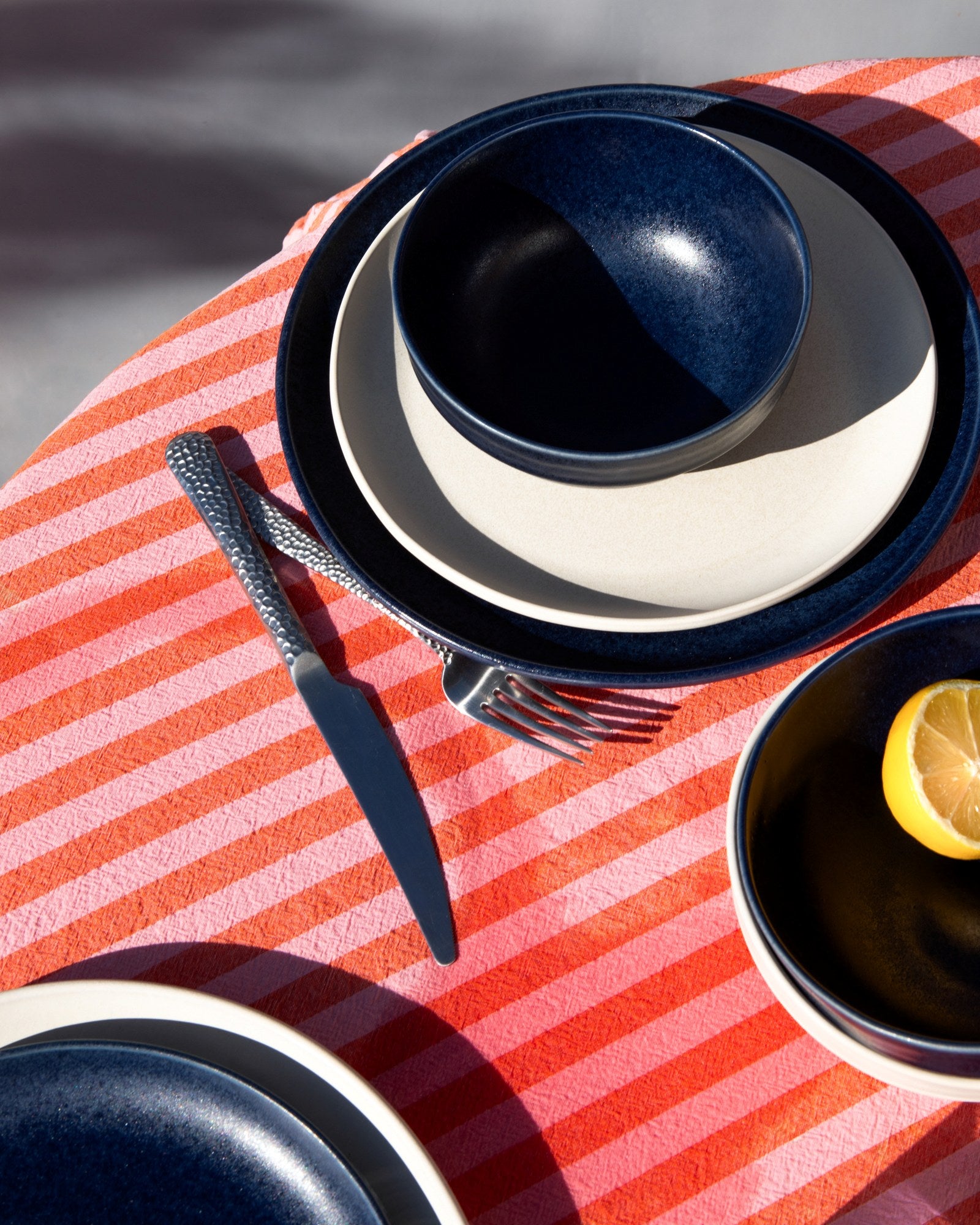 Tisch mit blauem und weißem Geschirr auf einem rot gestreiften Tuch, mit einem Messer, einer Gabel und einer Zitronenhälfte.