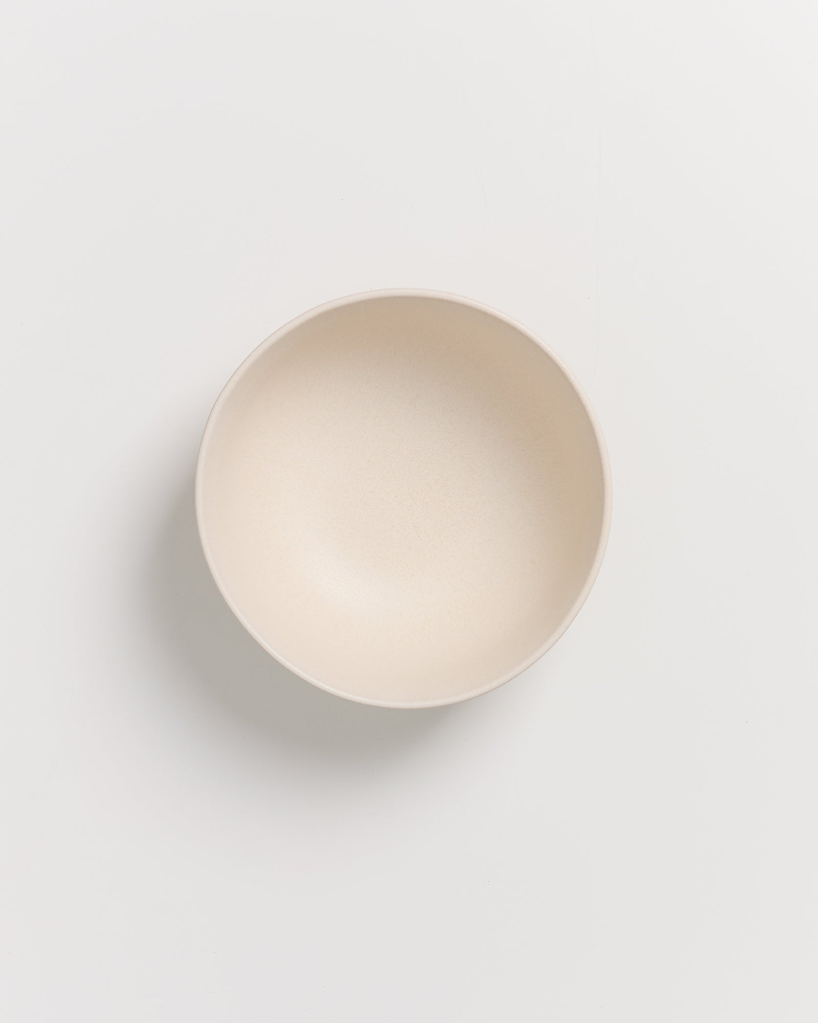 Beige Schüssel auf weißem Hintergrund, von oben betrachtet.