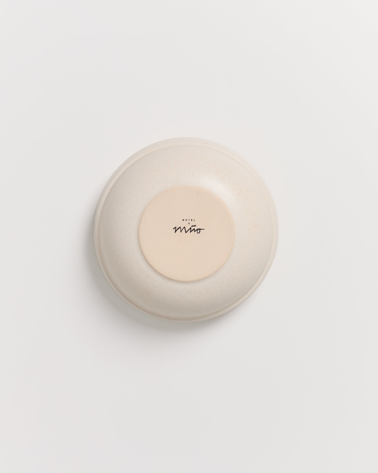 Beige Keramikschale auf weißem Hintergrund, mit schwarzem Schriftzug in der Mitte.