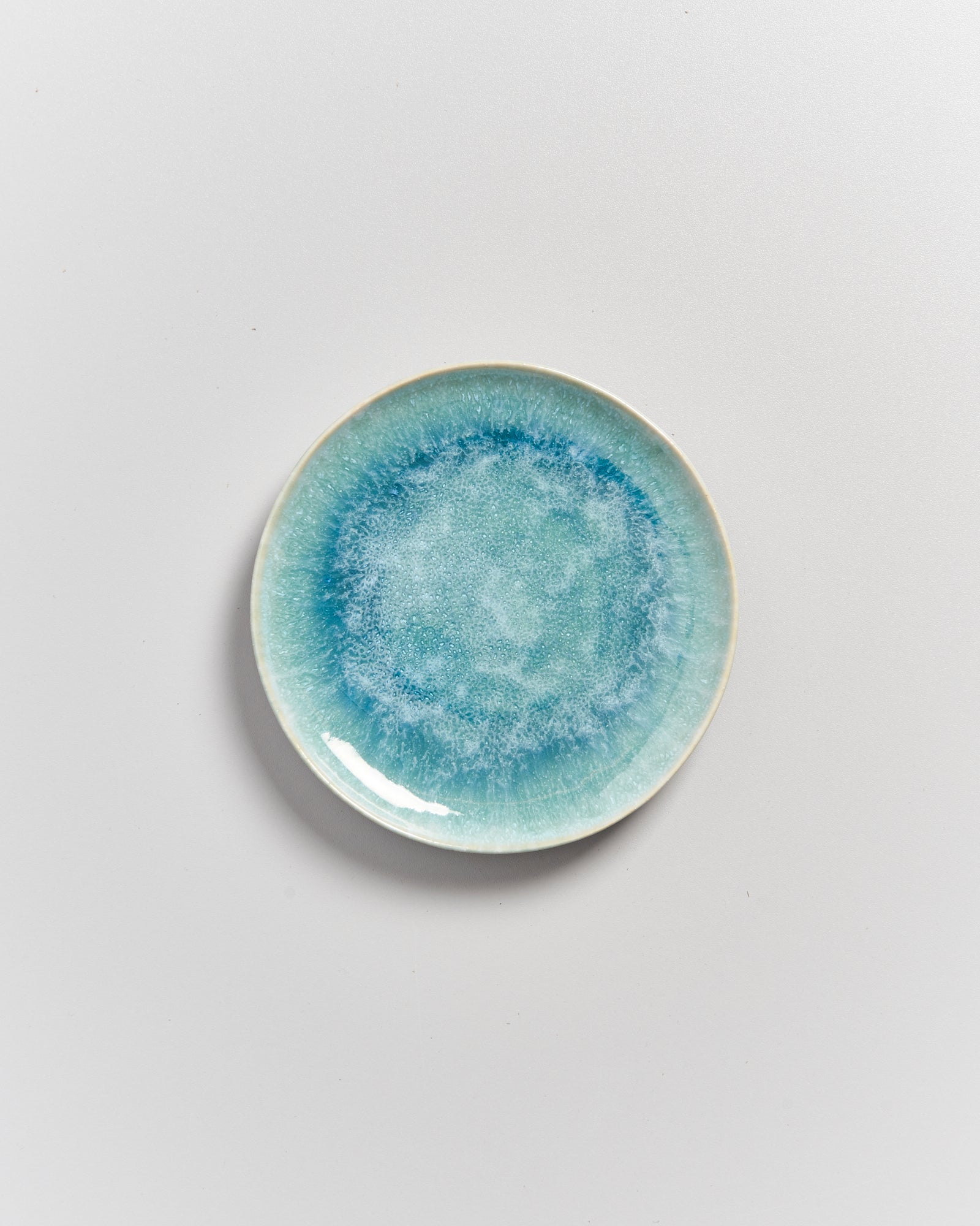 Eine runde blaue Keramikplatte mit einem aquarellähnlichen Muster auf einem weißen Hintergrund.