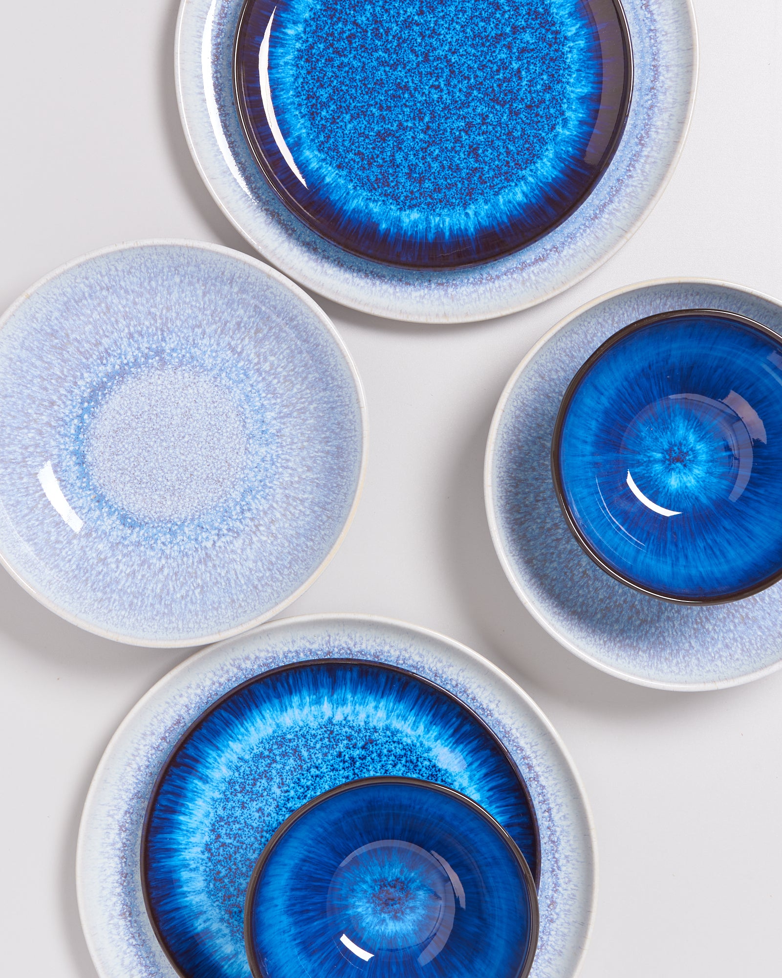 Fünf runde Keramikteller in verschiedenen Blautönen liegen auf einer weißen Fläche.